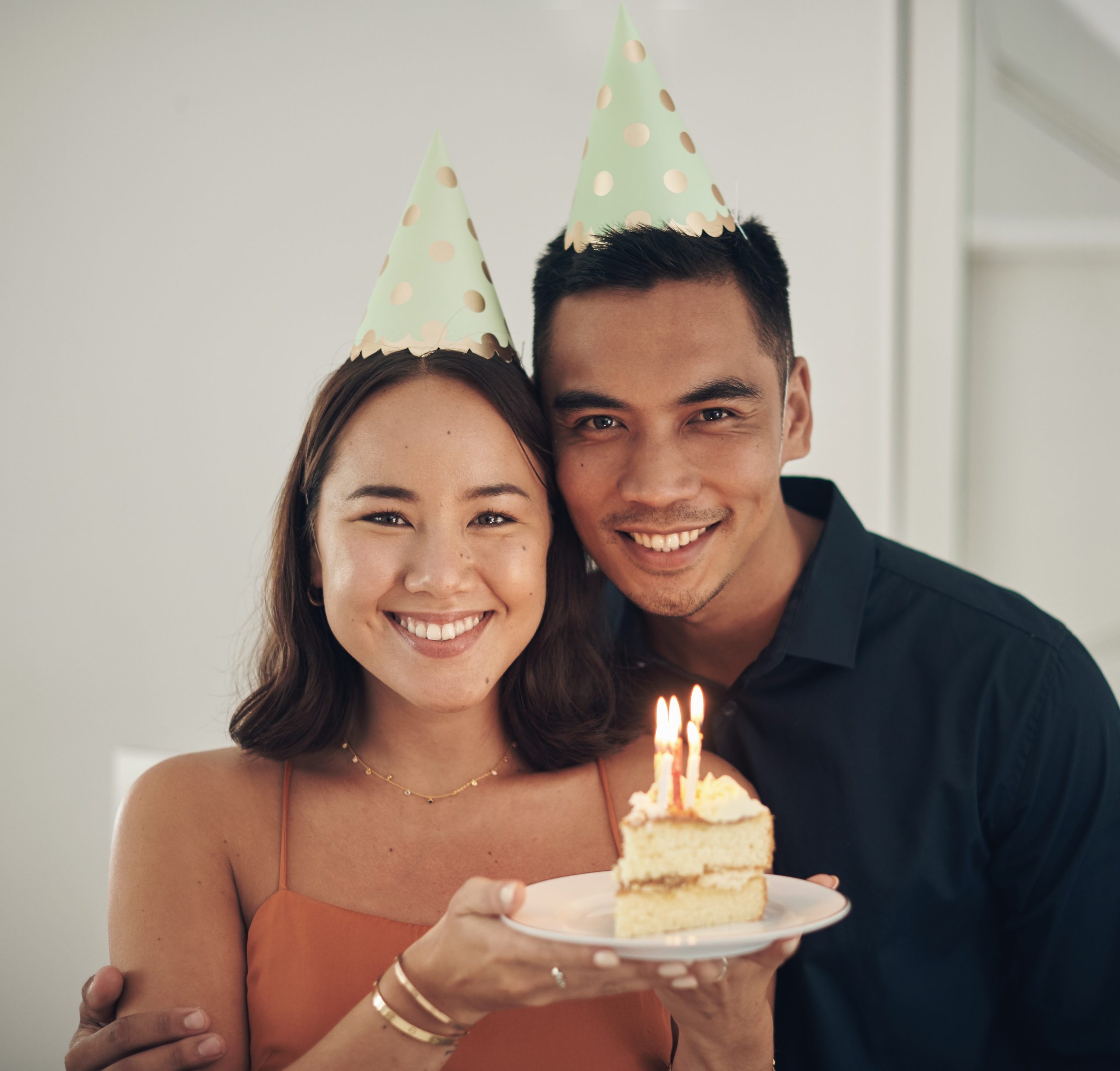 A couple poses for the camera with a piece of cake and party hats