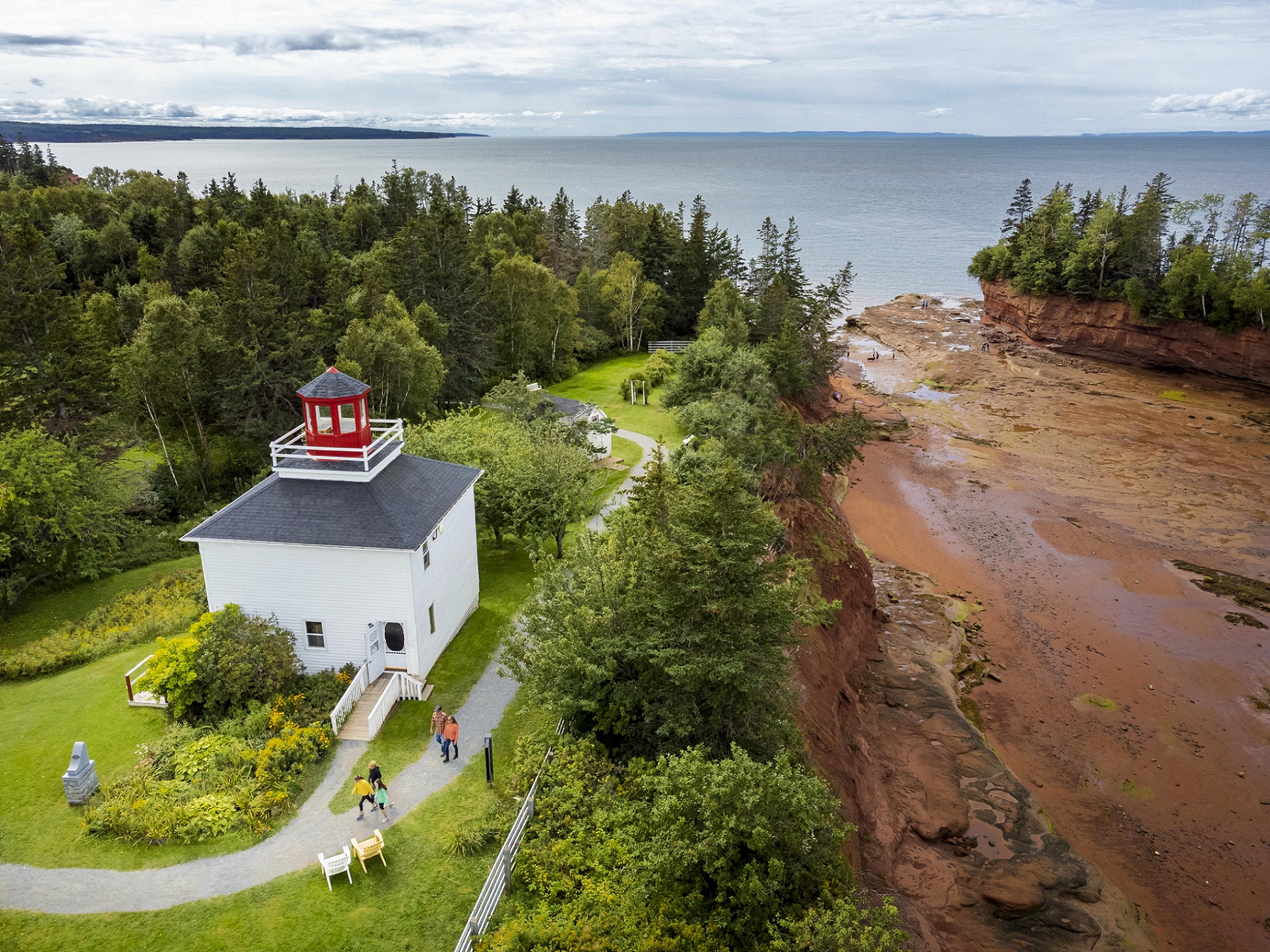 Burntcoat Head Lighthouse sits on the grassy edge of a cliff overlooking the ocean floor at low tide