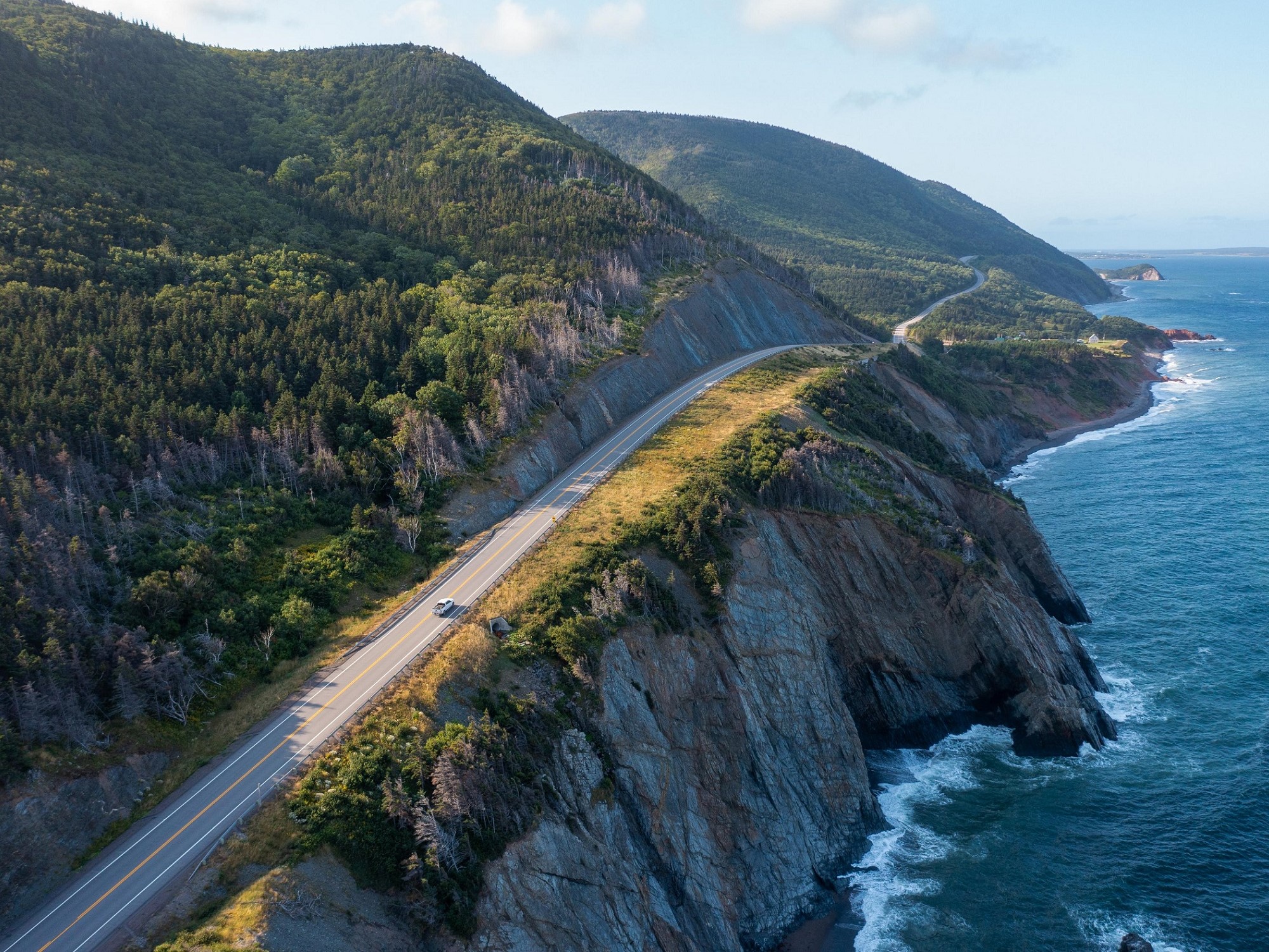 An aerial view of a car driving along the coastal roadway Cabot Trail