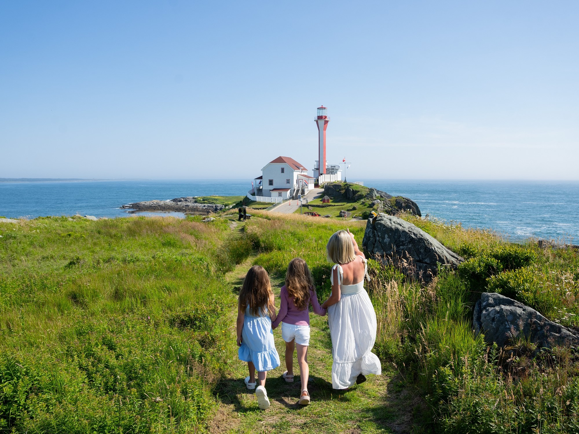 A mom and two daughters view the Cape Forchu lighthouse on the coast.