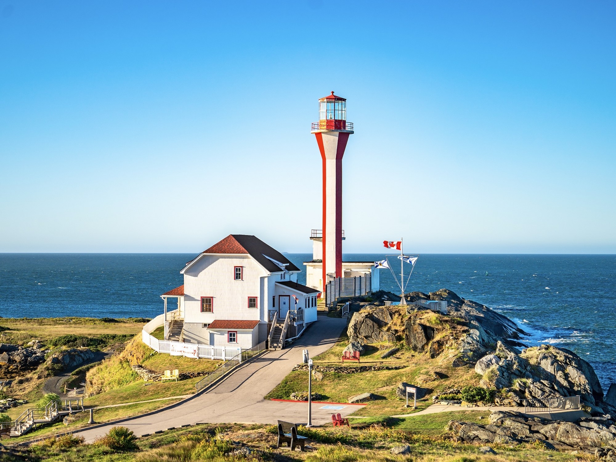 A red and white lighthouse is perched on a rocky shoreline overlooking the Atlantic Ocean.