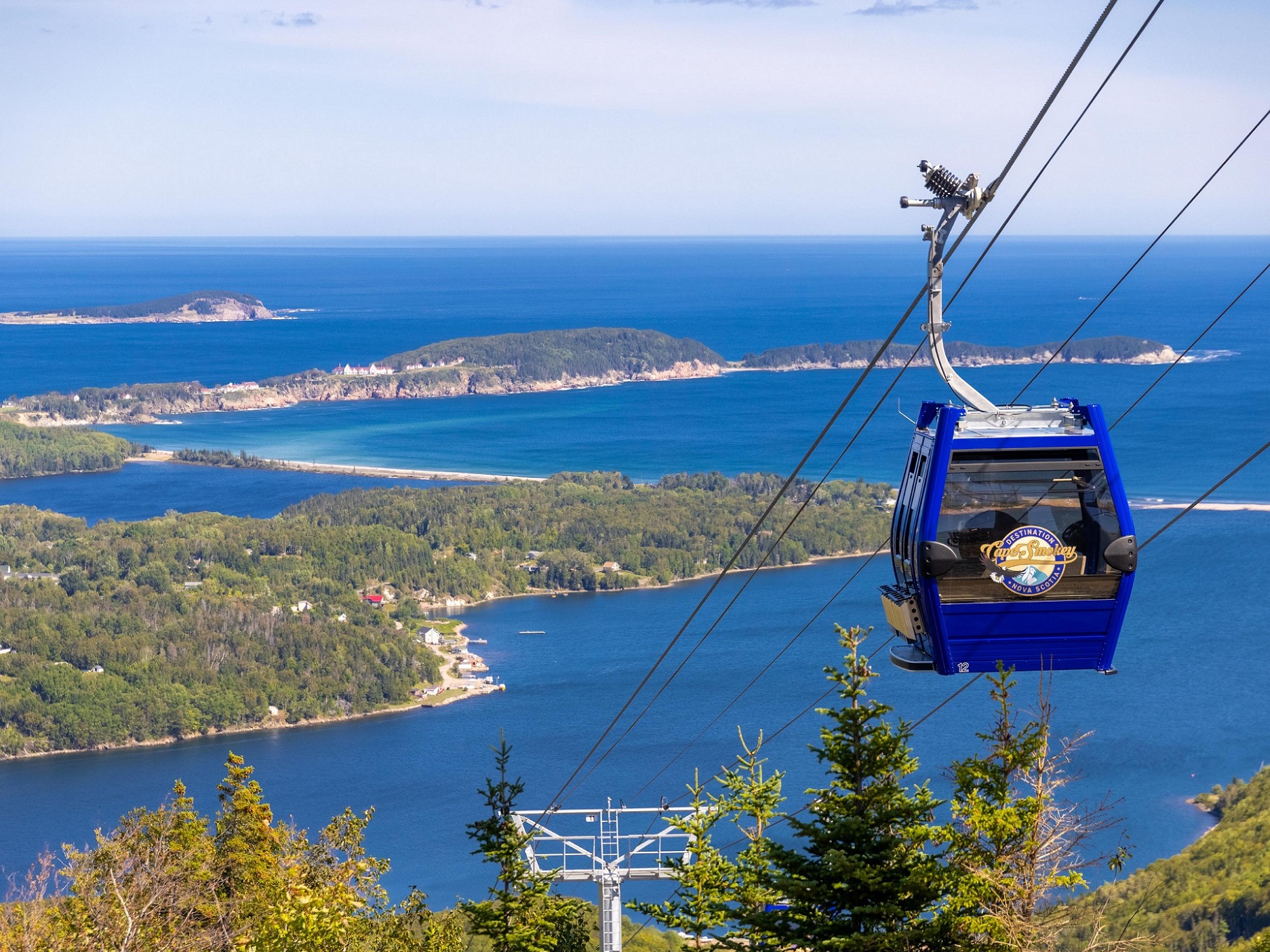 A blue gondola moves up a mountain looking out onto water views.