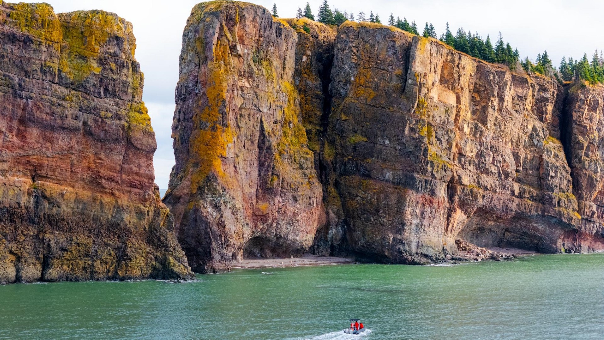 A small boat approaches towering cliffs during a tour.