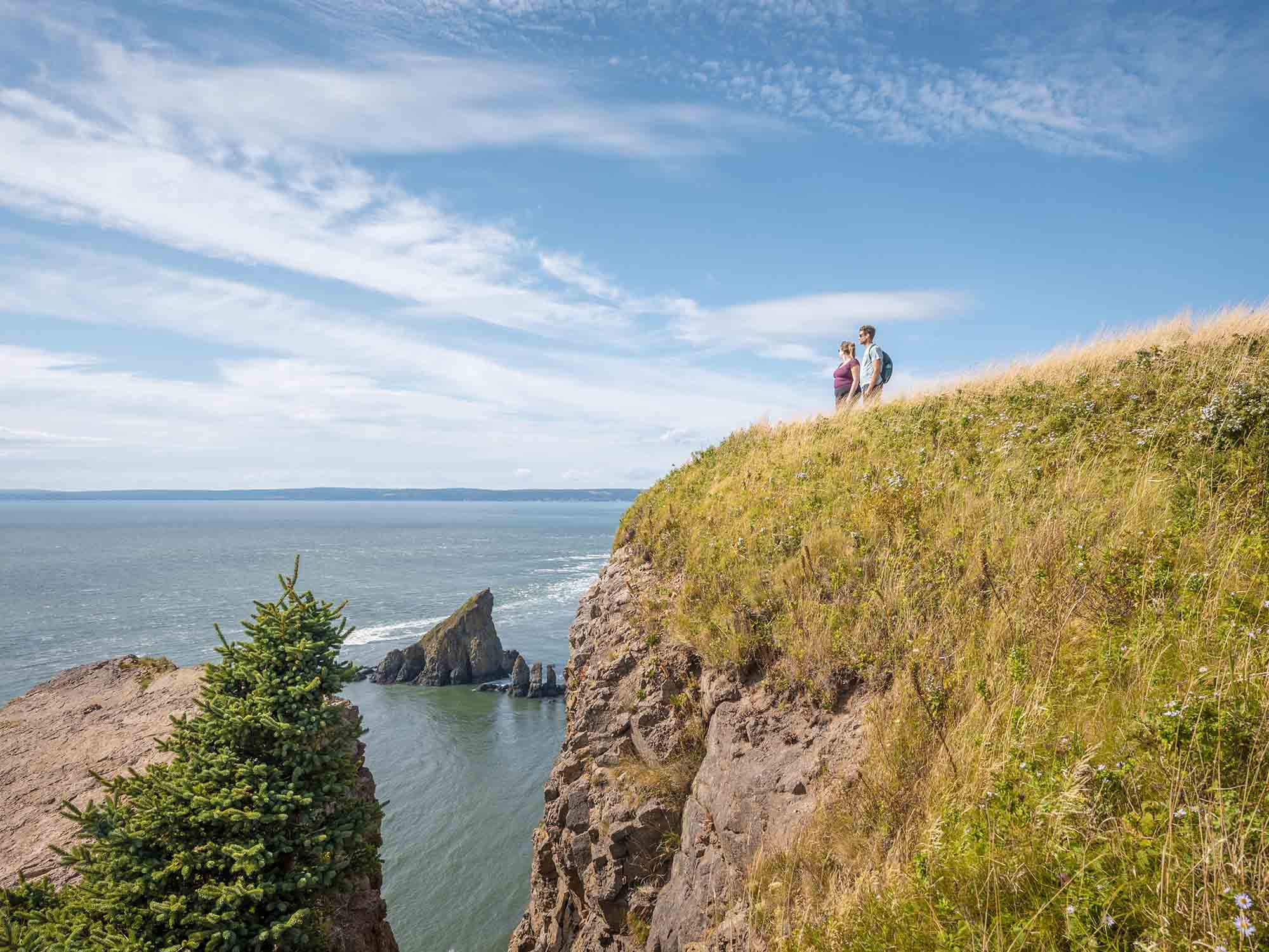 Two people experiencing the amazing view from the top of the Cape Split Trail, one of Nova Scotia's most popular hiking trails, over the rushing Bay of Fundy Tides in the Annapolis Valley.