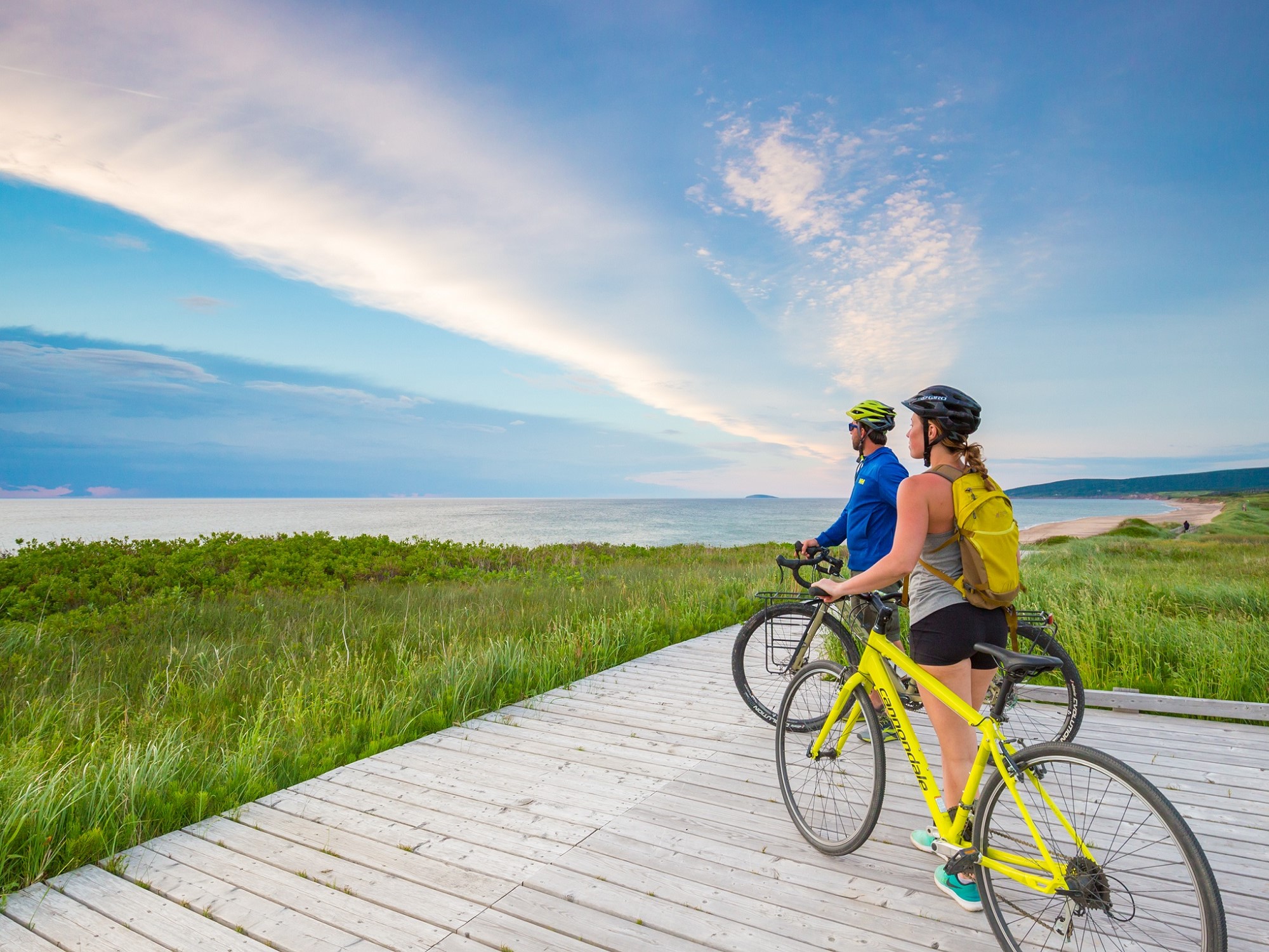 Two cyclists take a rest and are standing with their bikes looking out at the water.