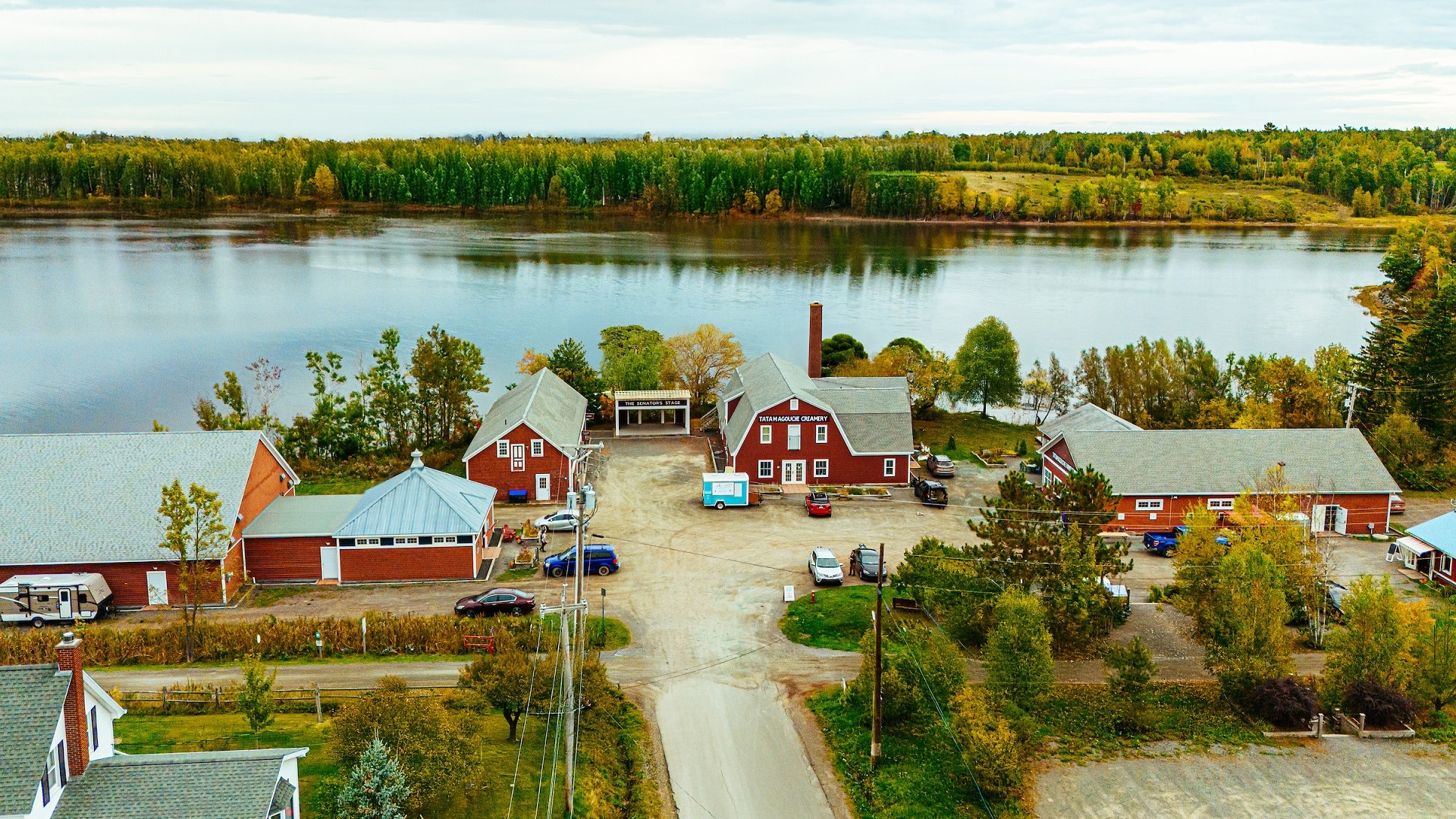 An aerial view of red buildings next to a river with fall colours in the background.