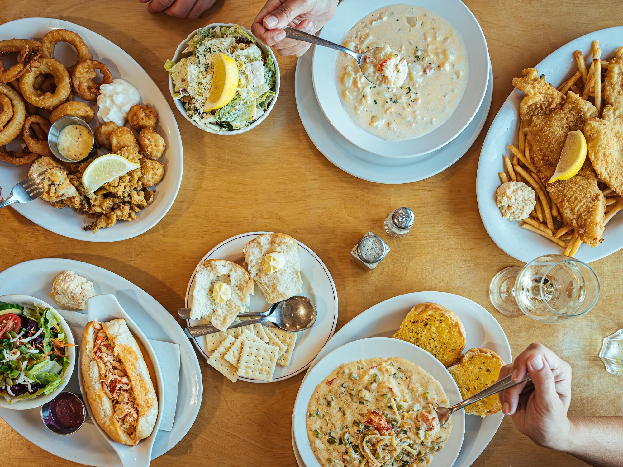 An overhead view of a table of food including seafood chowder, seafood pasta, a lobster roll and other fried seafood.