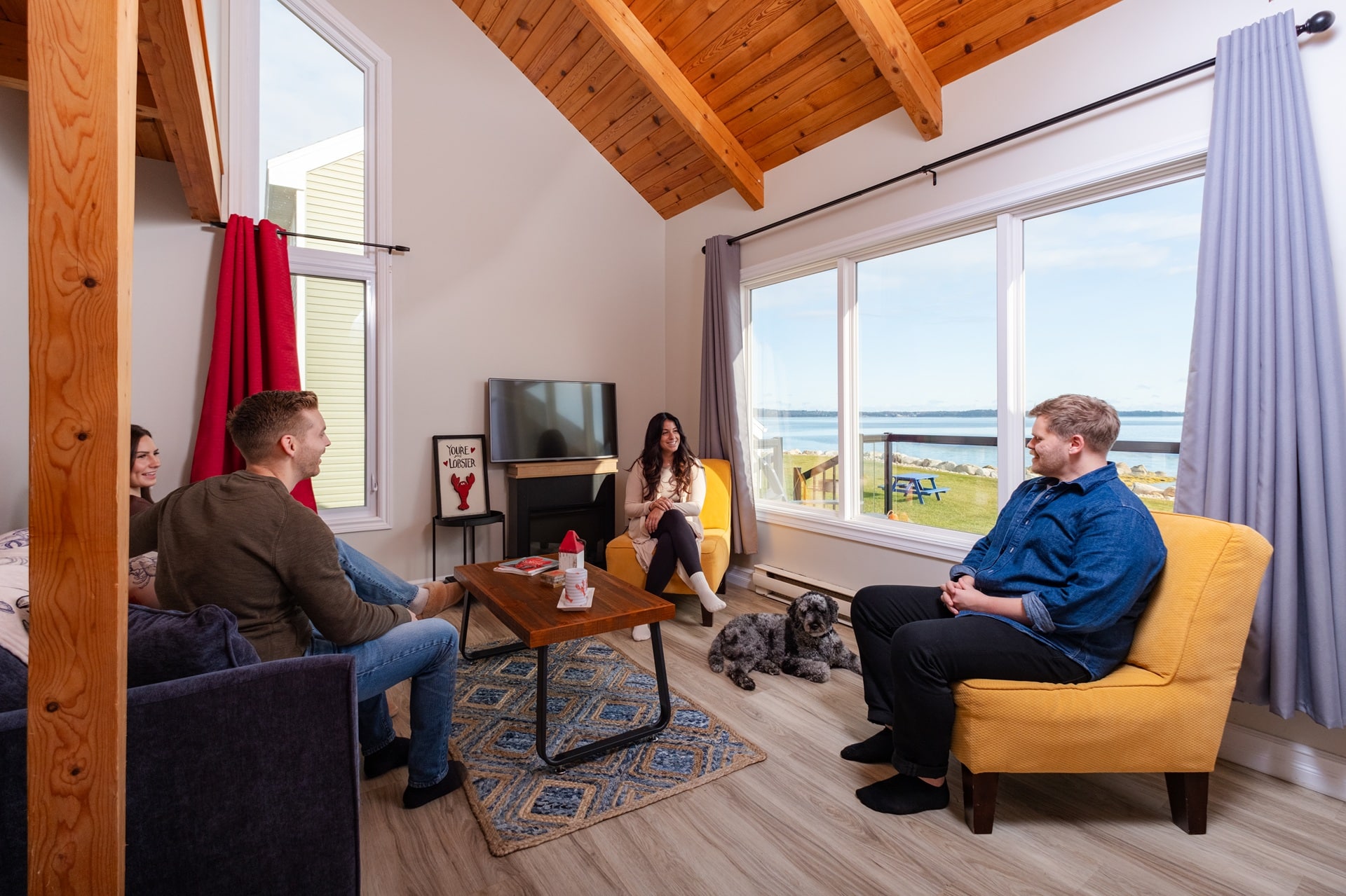 Three people sit inside a cottage. Out the window you can see the ocean.