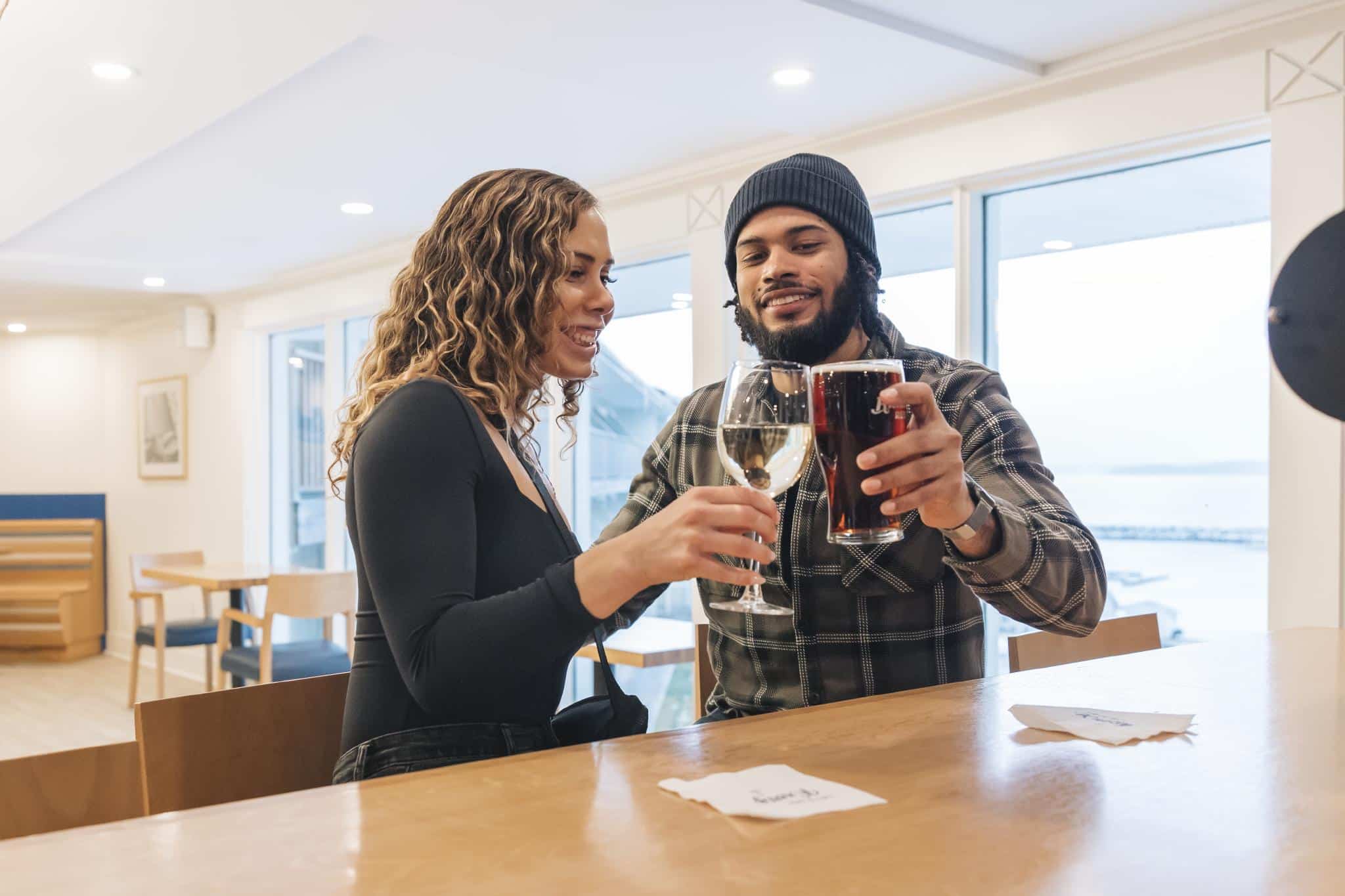 Two people cheers their beer at a high top bar.