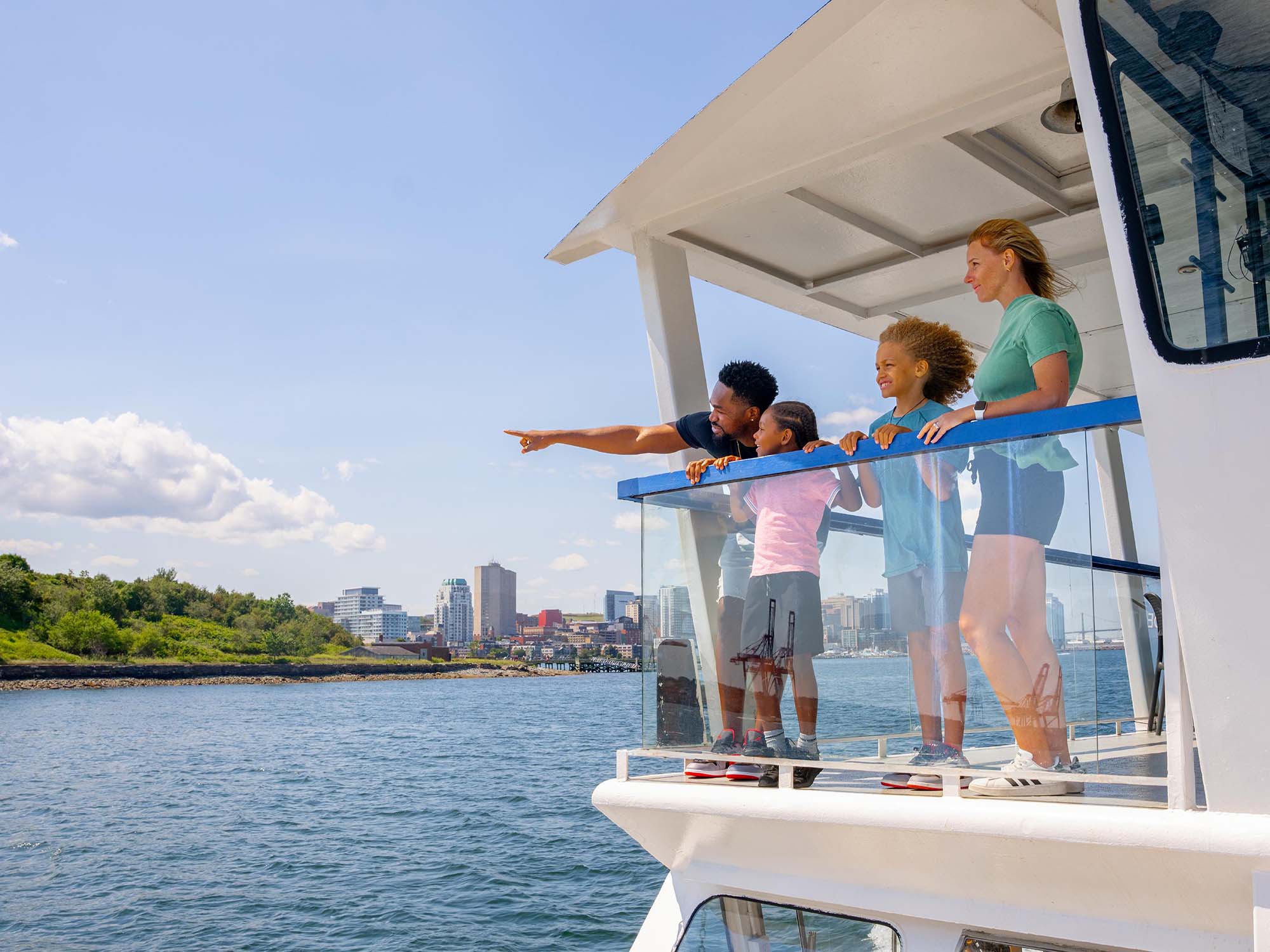 Parents and their two children pointing at the wharf on Georges Island National Historic Site from the water taxi taking them there from the Halifax Waterfront for a fun day in Nova Scotia