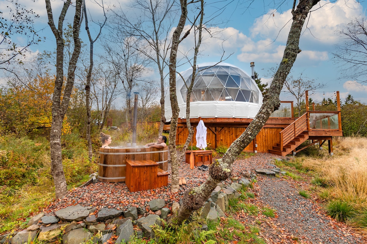 A person stands outside a dome during fall. The dome sits on a wooden platform and the person is in a white robe.