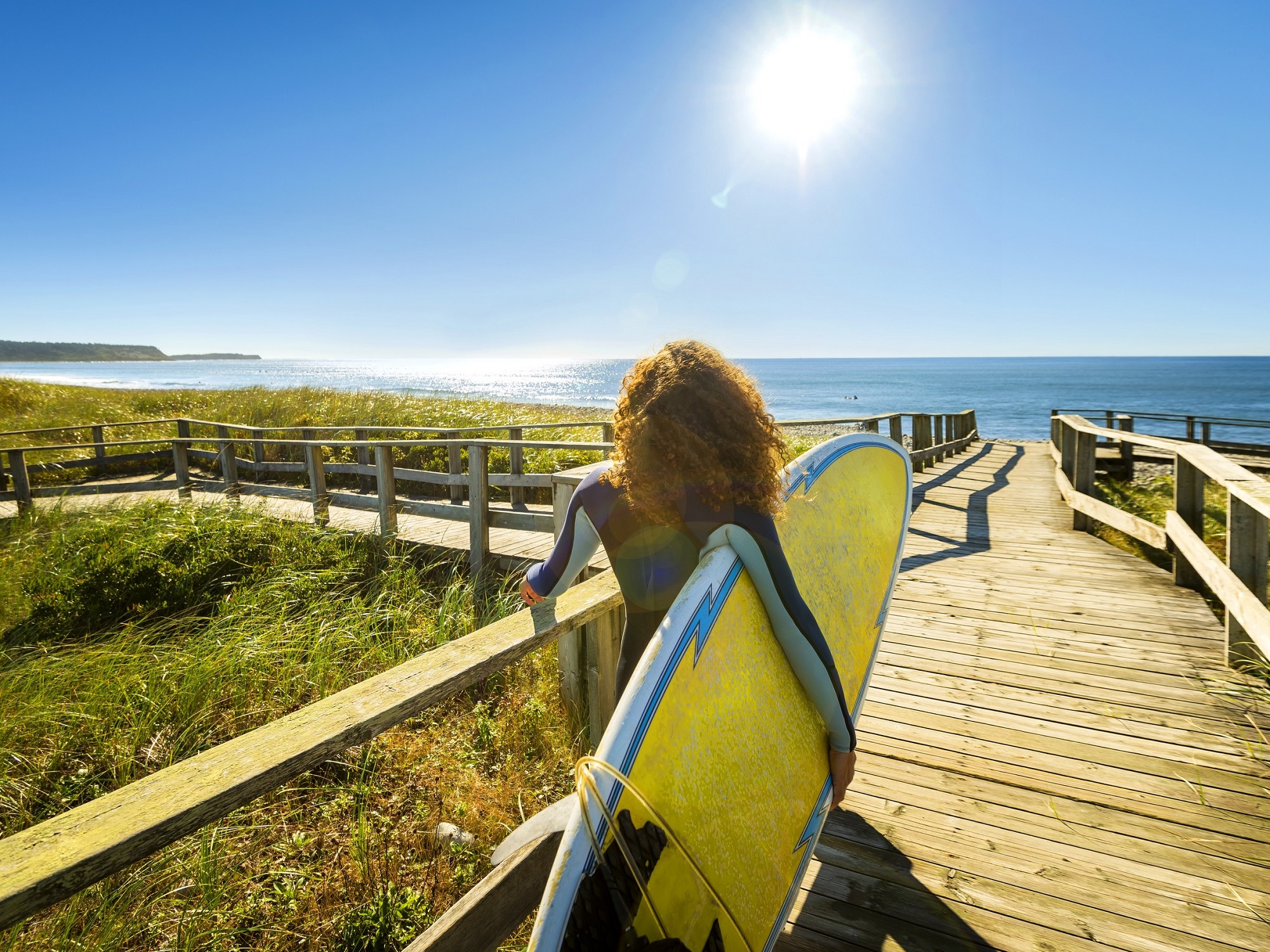 A woman stands with her surfboard looking out into the ocean.