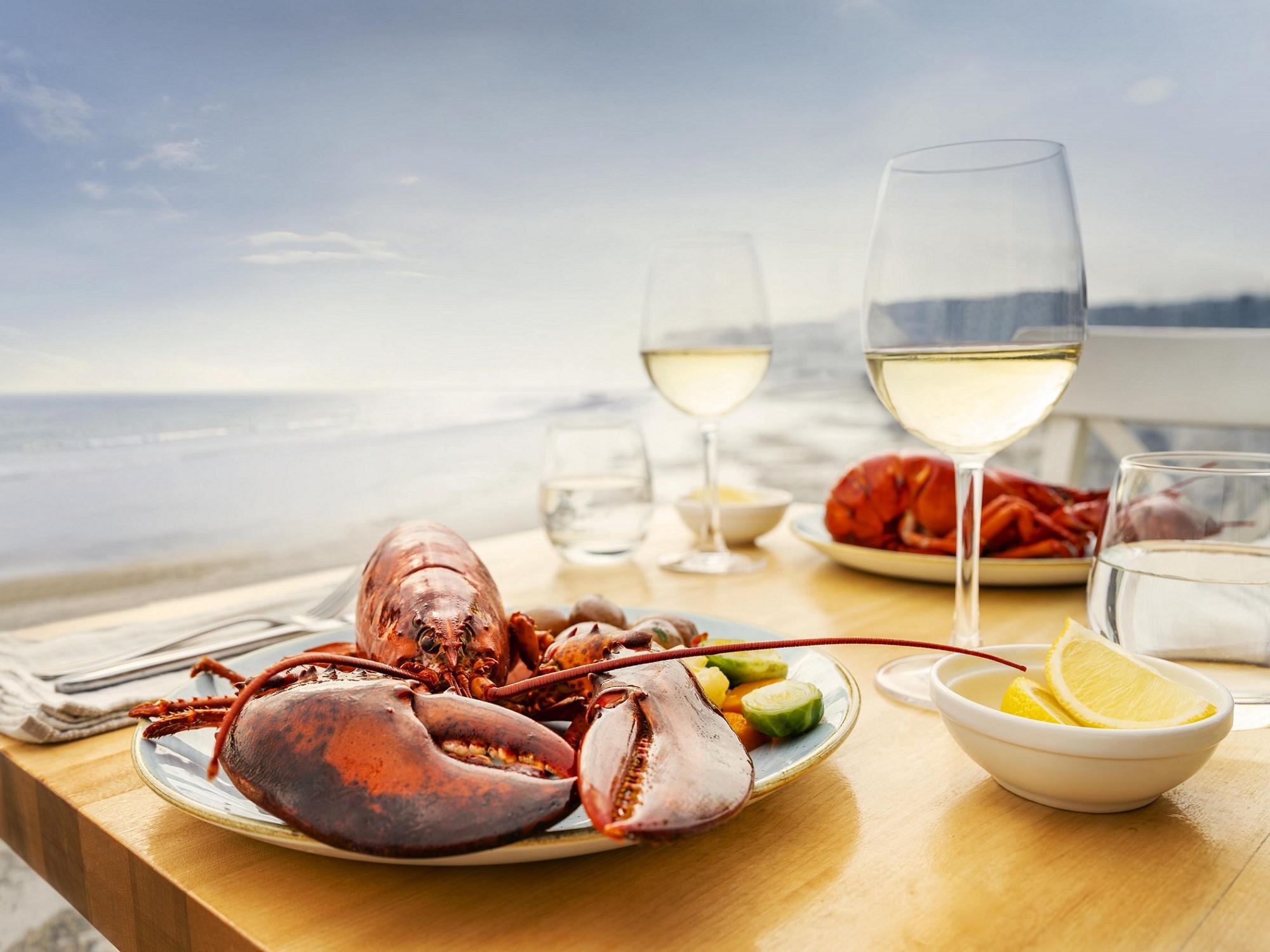 A lobster dinner on a plate with a glass of white wine next to it.