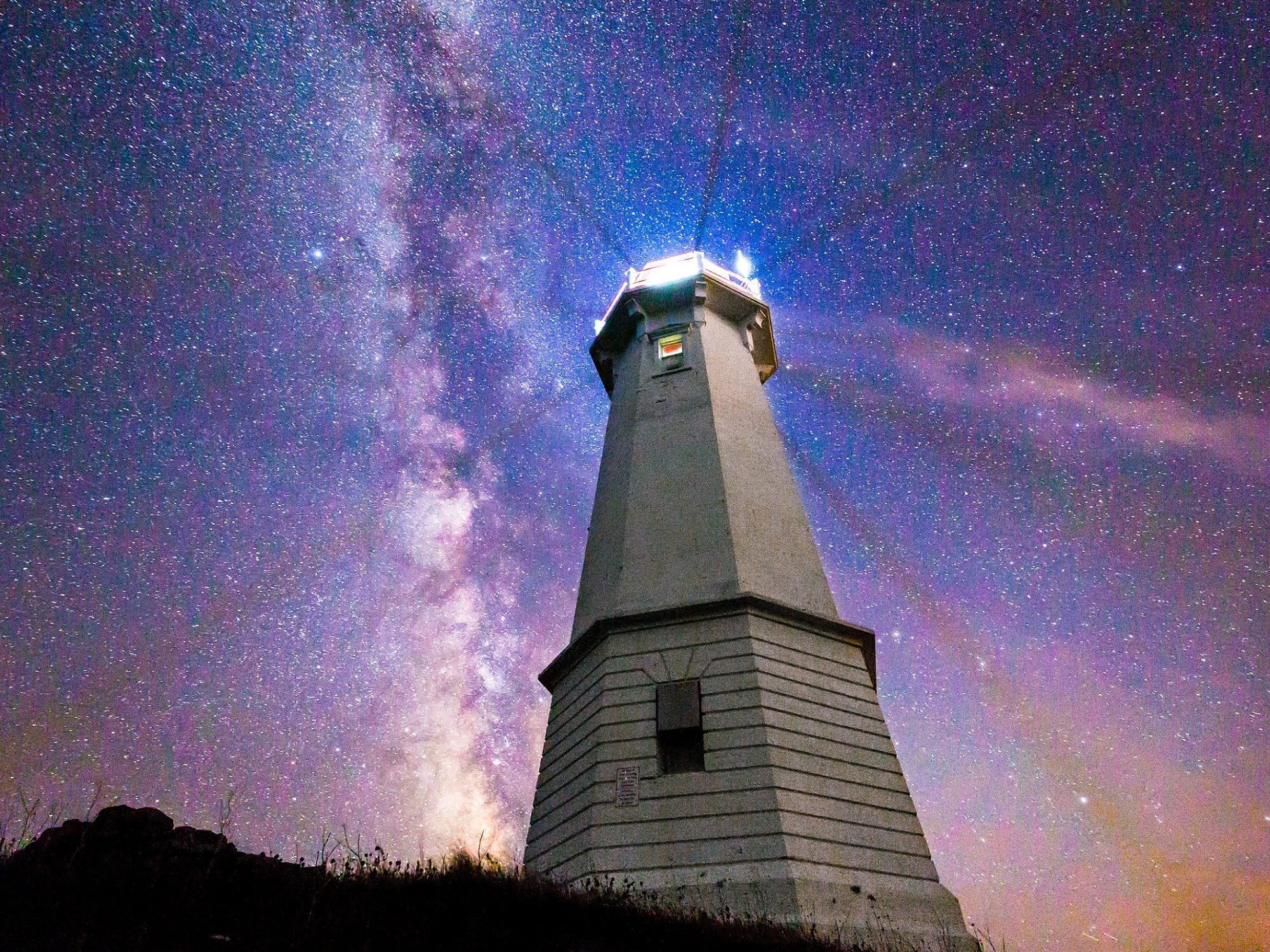 Louisbourg Lighthouse with its beacon shining beneath a starry sky.