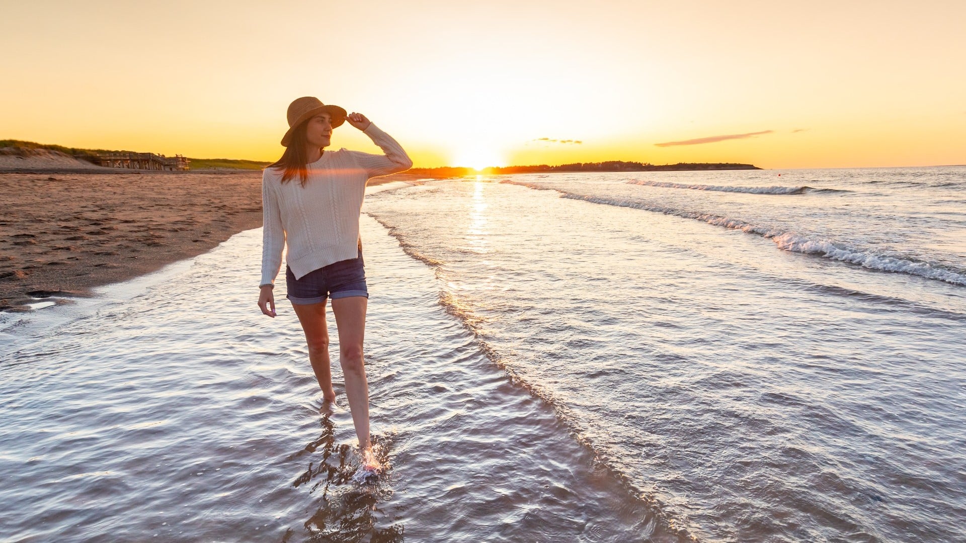 A woman walks along the beach at sunset