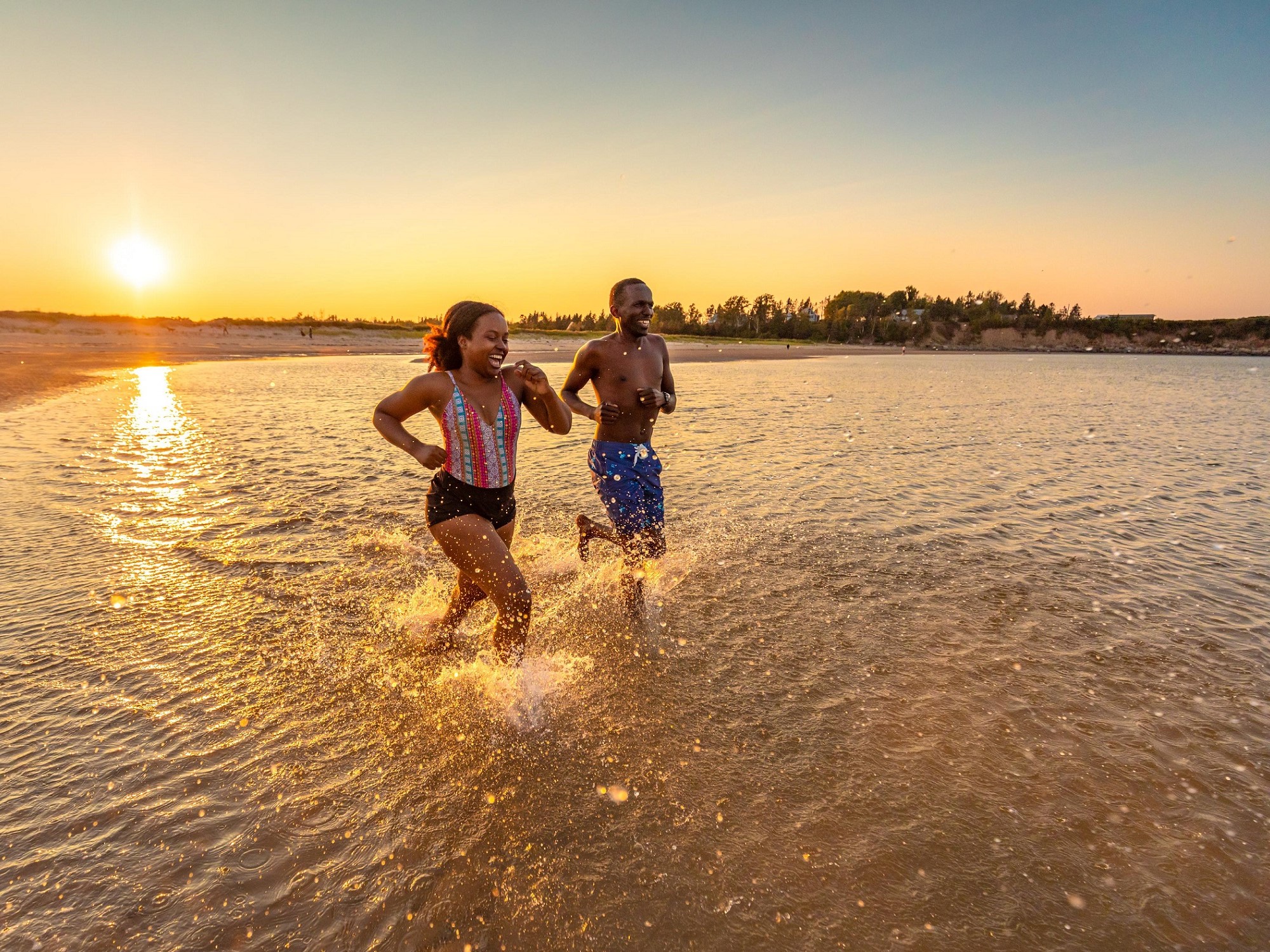 Two people run into the water for a swim during sunset.