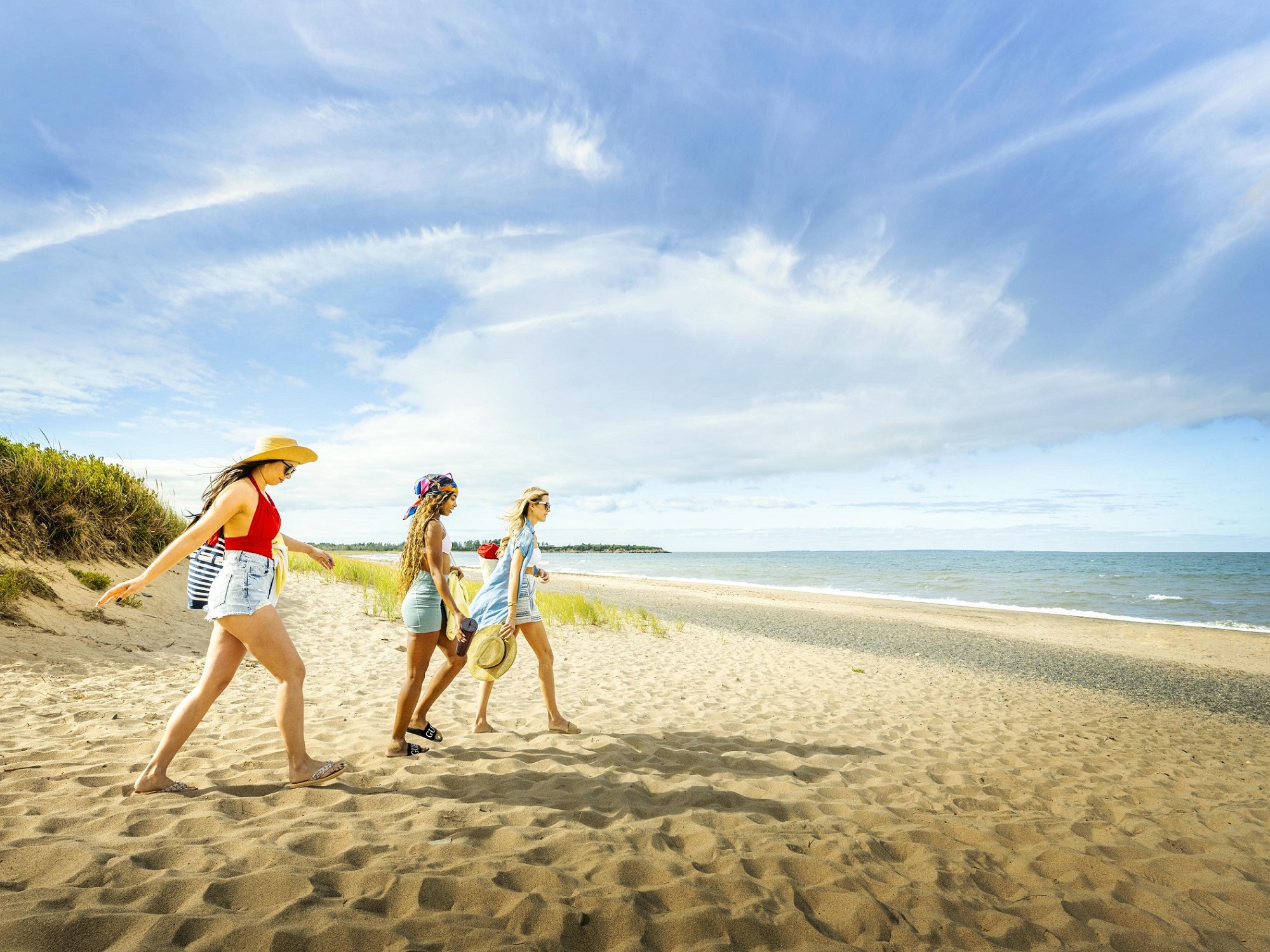 Three women walk on the beach ready for a beach day.