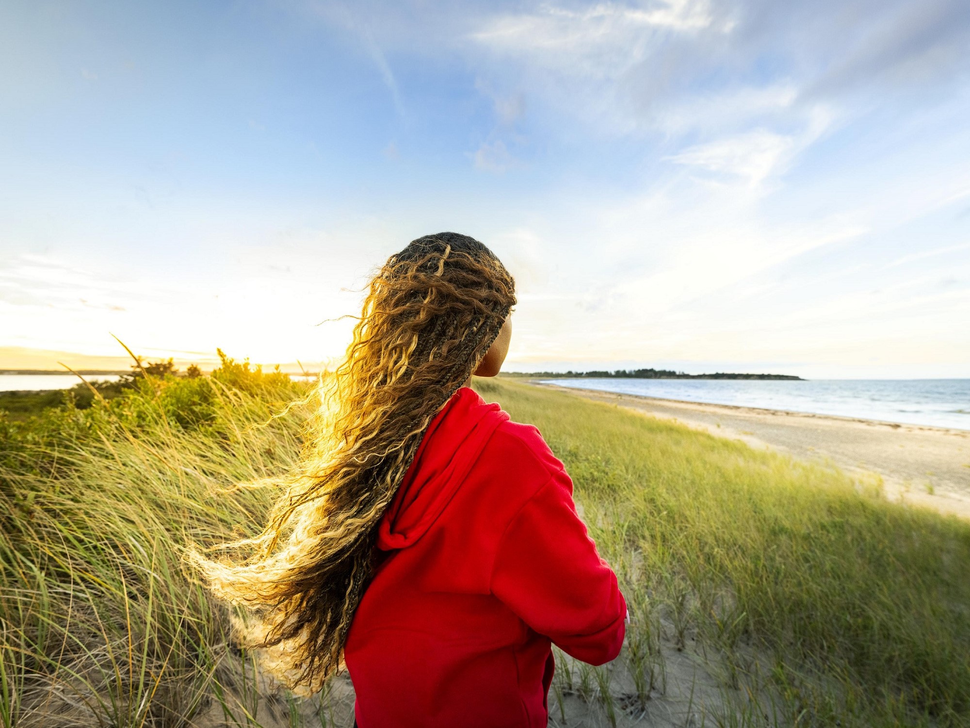 A woman wearing a red hoodie looks out onto a sandy beach and blue water at Melmerby Beach Provincial Park.