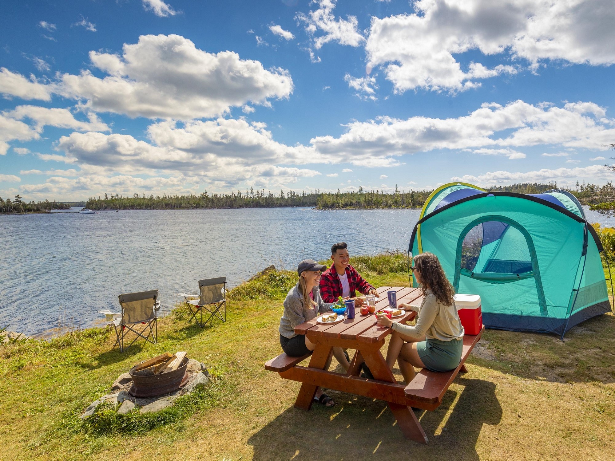 Three people eat at a picnic table next to their campsite and the ocean.
