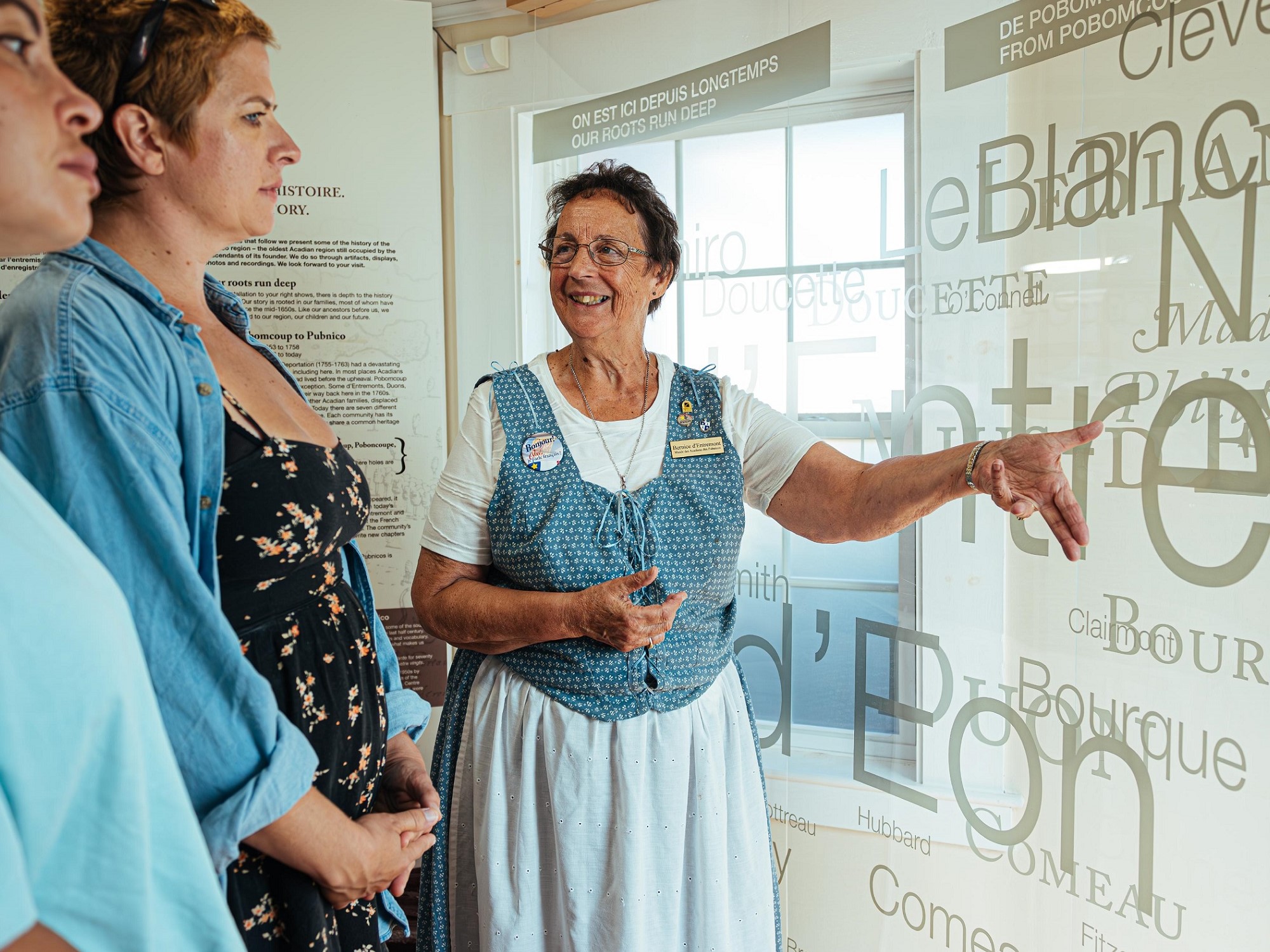 A museum interpreter points to a display about Acadian culture as two museum guests look on.