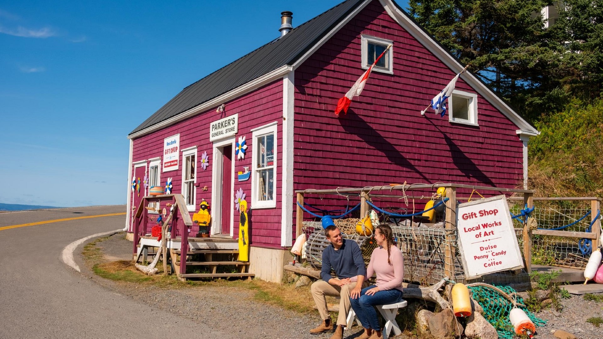 Two people sit on a bench outside a maroon coloured rustic gift shop.