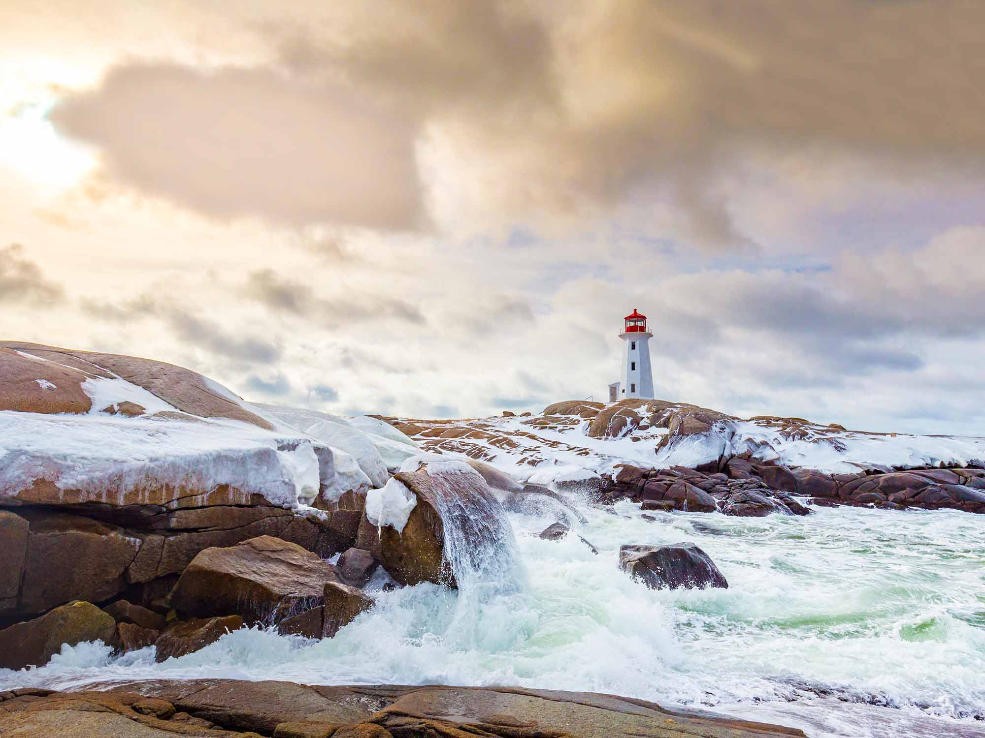 View of Peggy's Cove in winter with rough ocean and clouds clearing and some sunshine popping through in Nova Scotia