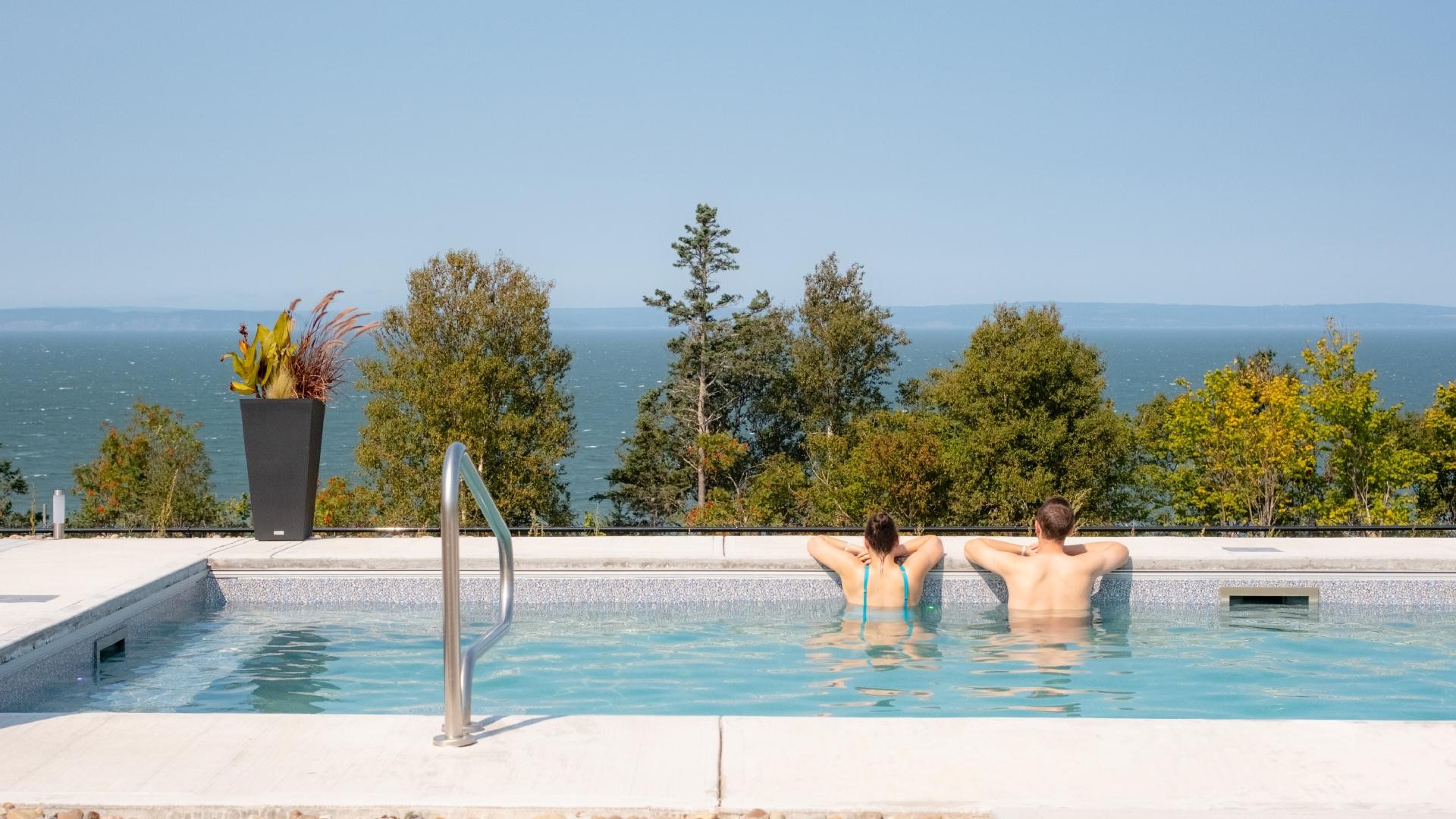 Two people have their backs to the camera as they relax in a Nordic spa pool overlooking the Bay of Fundy.