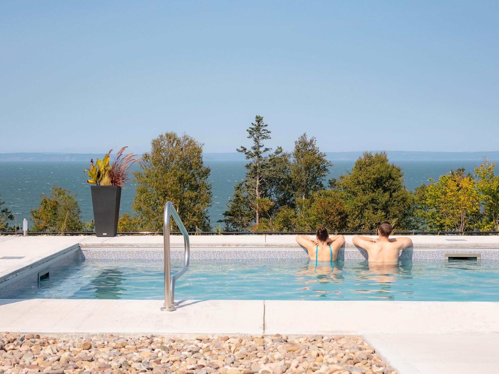 Two people leaning on the edge of the hot pool as they overlook the Bay of Fundy from Saltair Nordic Spa in Baxter's Harbour, Nova Scotia