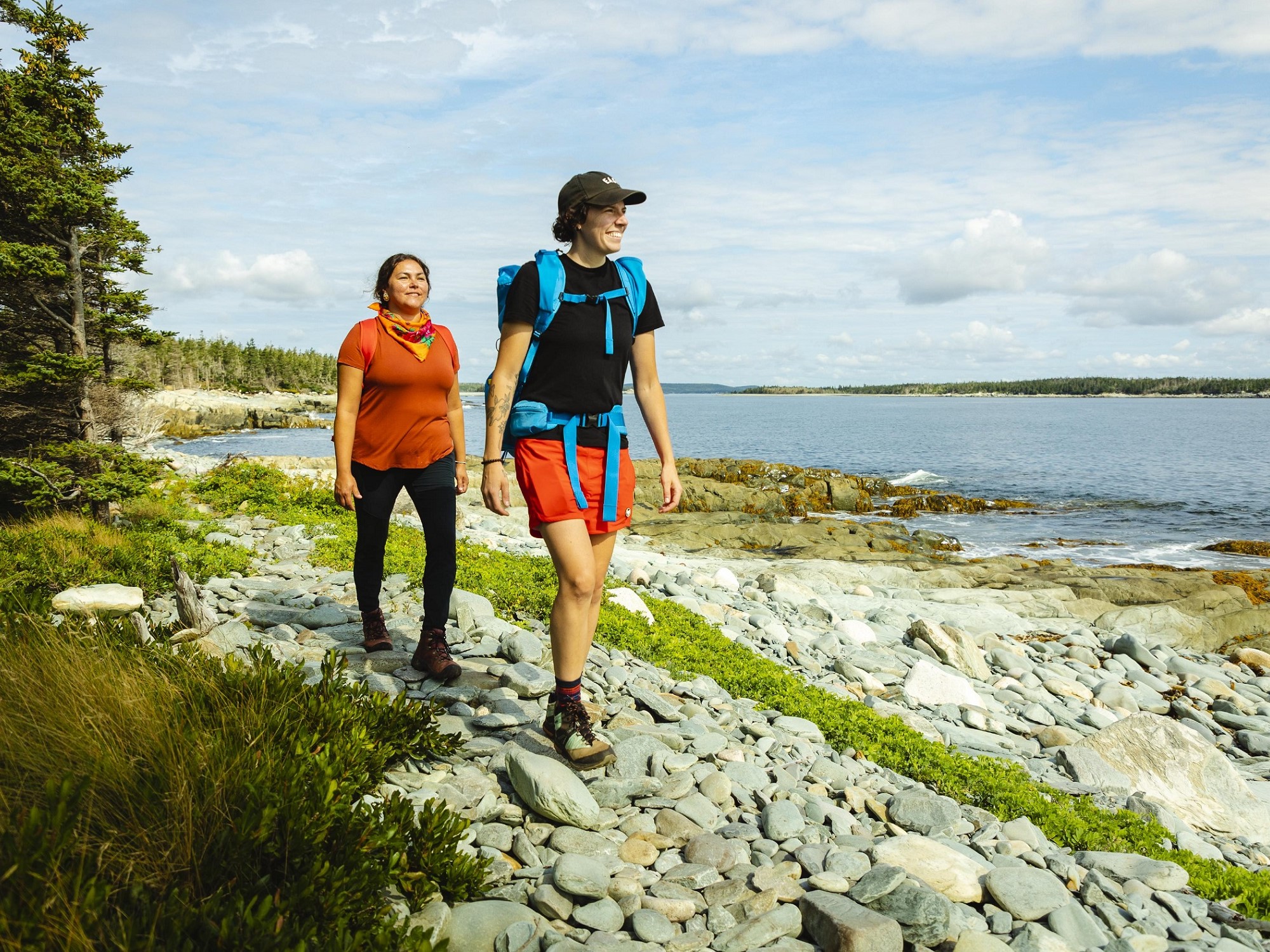 Two people hike along a rocky shoreline next to the ocean.