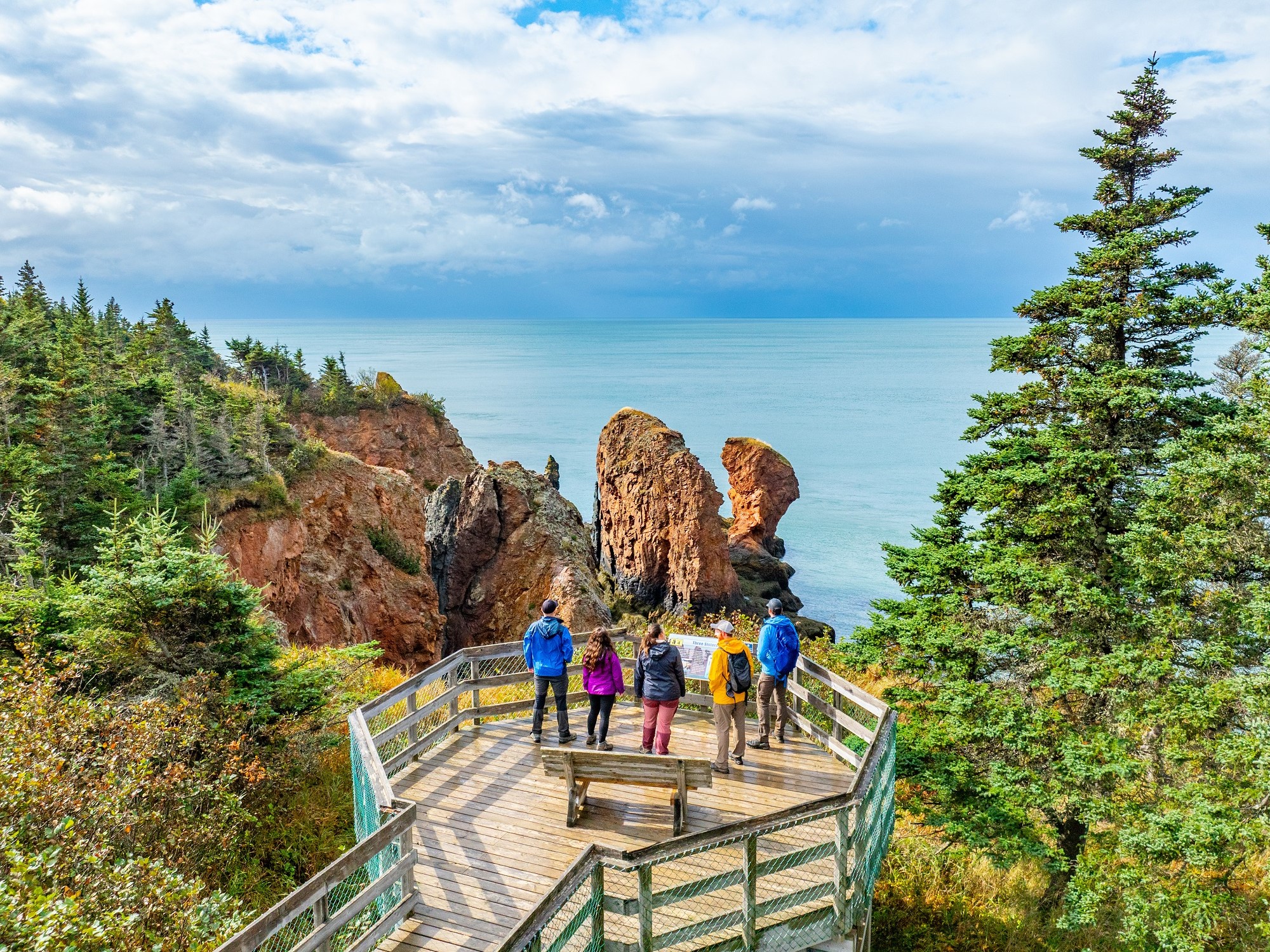 Three people observe the Three Sisters rock formation from a platform overlooking the Bay of Fundy on a tour with Local Guy Adventures.