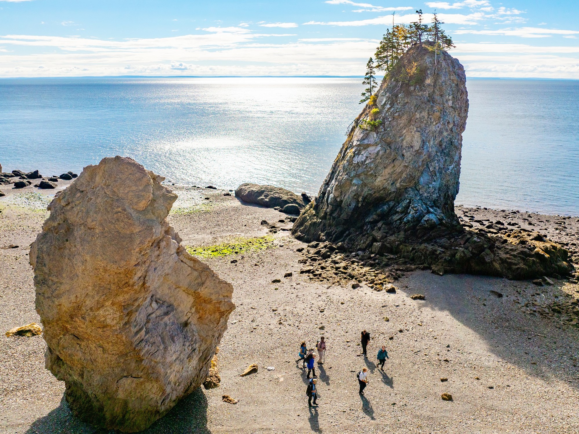 An aerial view of giant rock formations and people looking small on the beach below on a tour with Tide Rollers and Mud Larkers