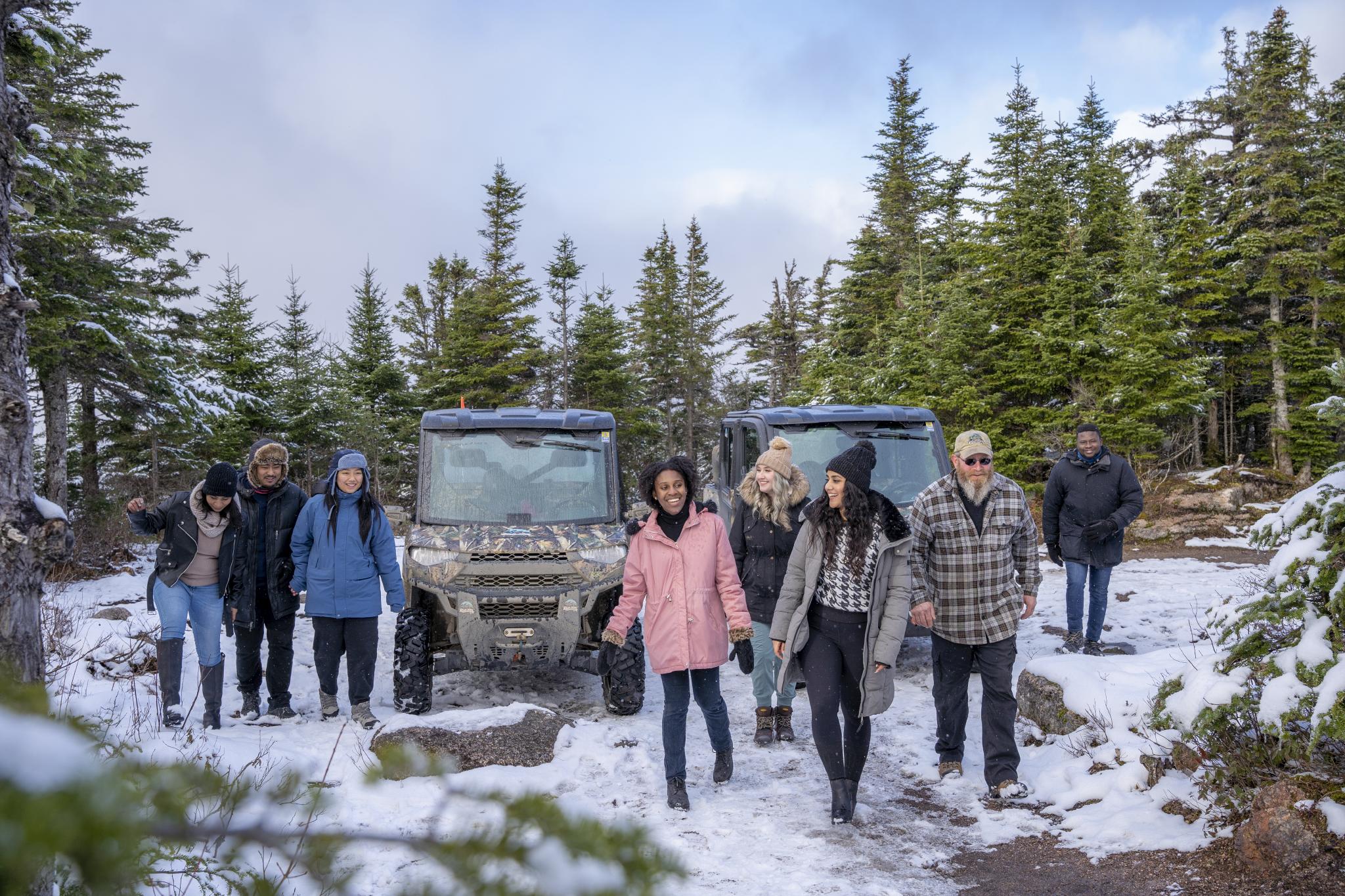 A group of people are walking the woods in winter after exiting a side by side on a TNT group tour.