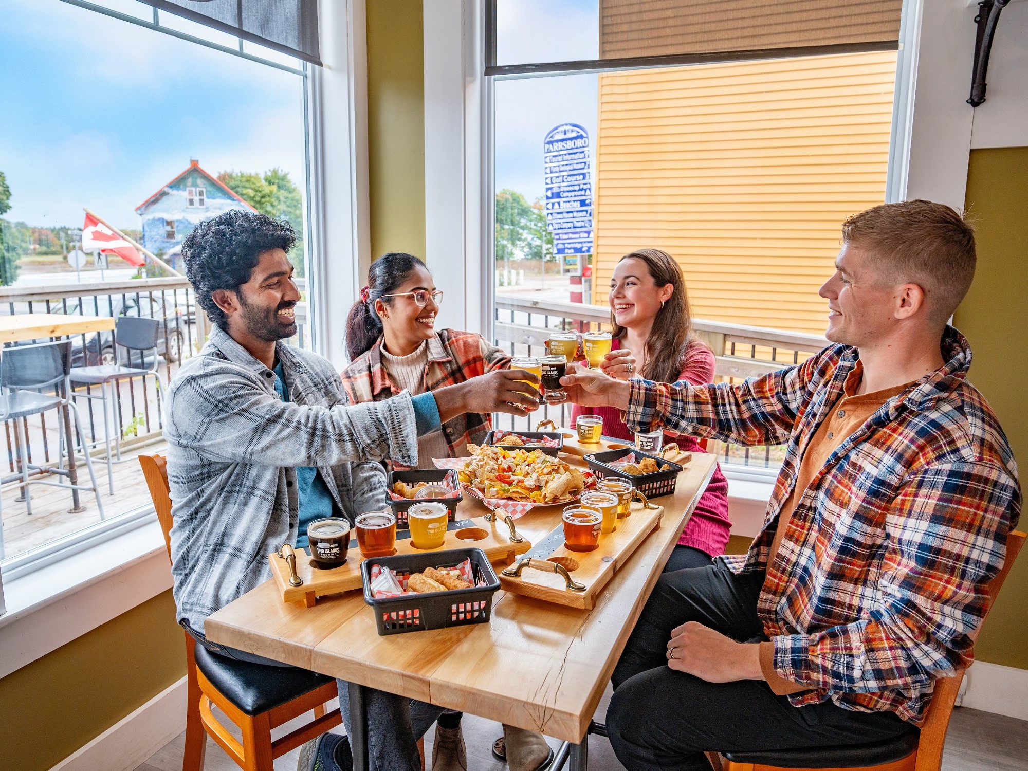 Four friends do a cheers over a table of food and beer at Two Islands Brewing