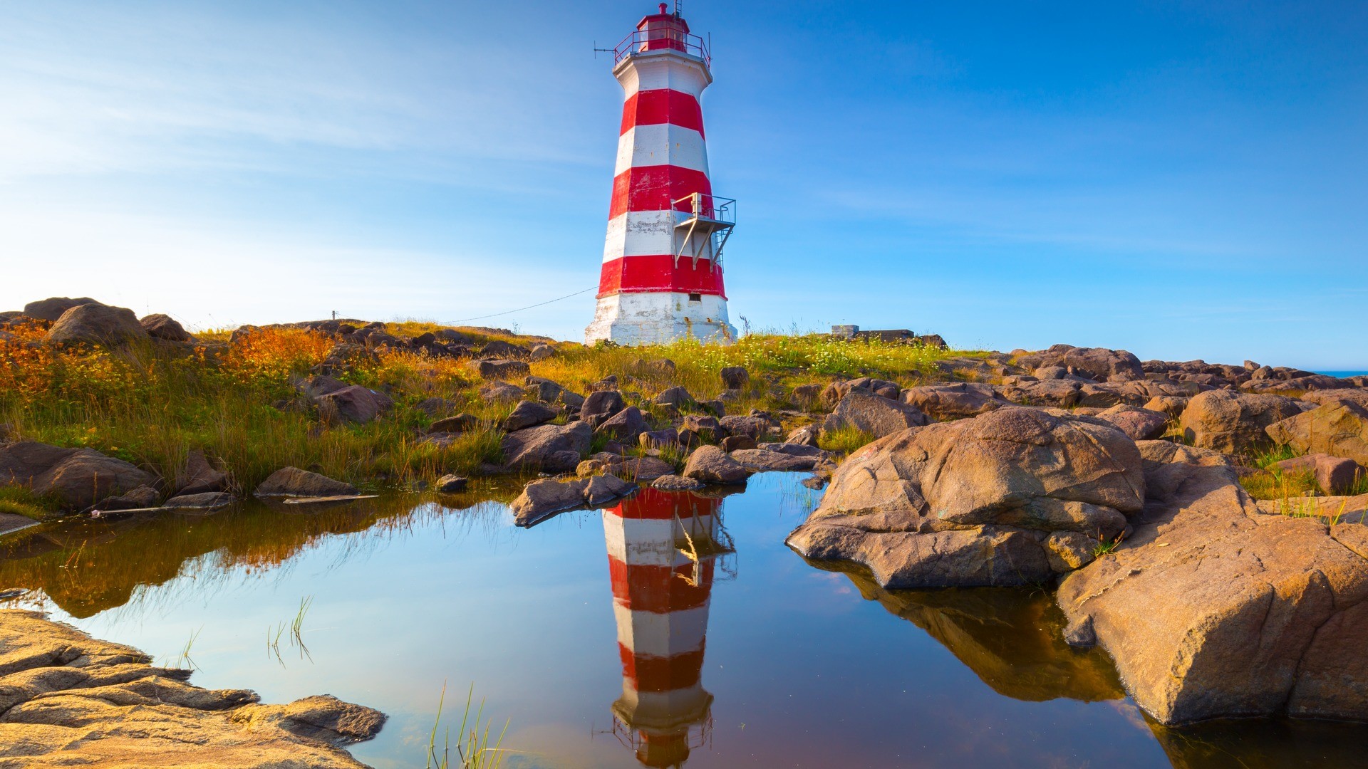 A red and white striped lighthouse on a blue sky day