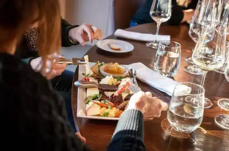 Focused on a person's hands, eating a meal. There are wine glasses on the wooden table.