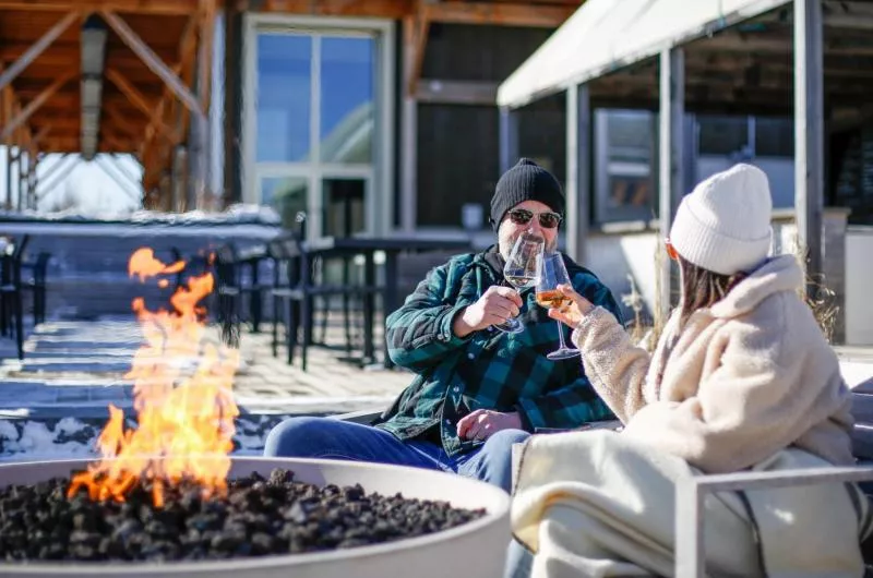 Two people cheers wine outside at a firepit.