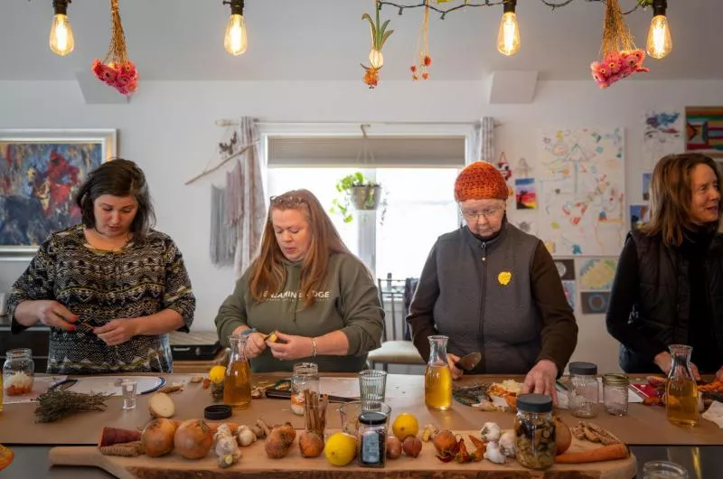 A group of four people are standing at a table and look to be prepping vegetables.