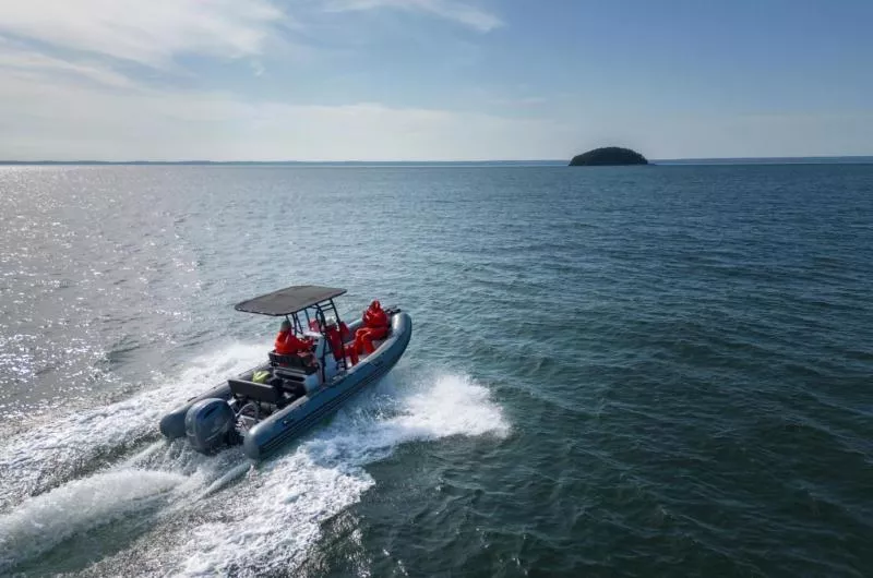 A small but fast boat is heading out on the water toward a tiny island in the distance. It is a sunny day.
