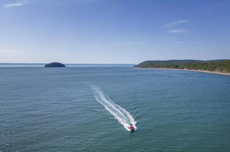 A zodiac style boat speeds through the Bay of Fundy leaving a small island in the distance. It is a sunny, blue sky day.