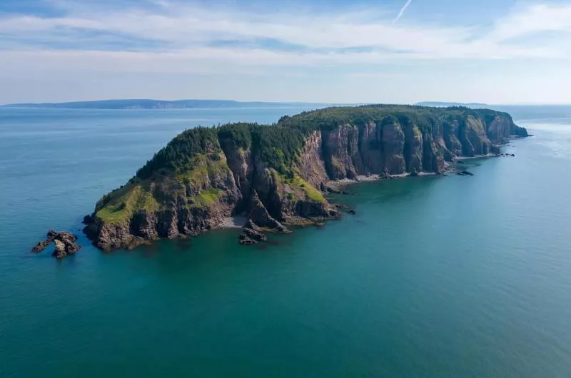 A large, narrow area of land with tall cliffs juts out into the blue water of the Bay of Fundy.