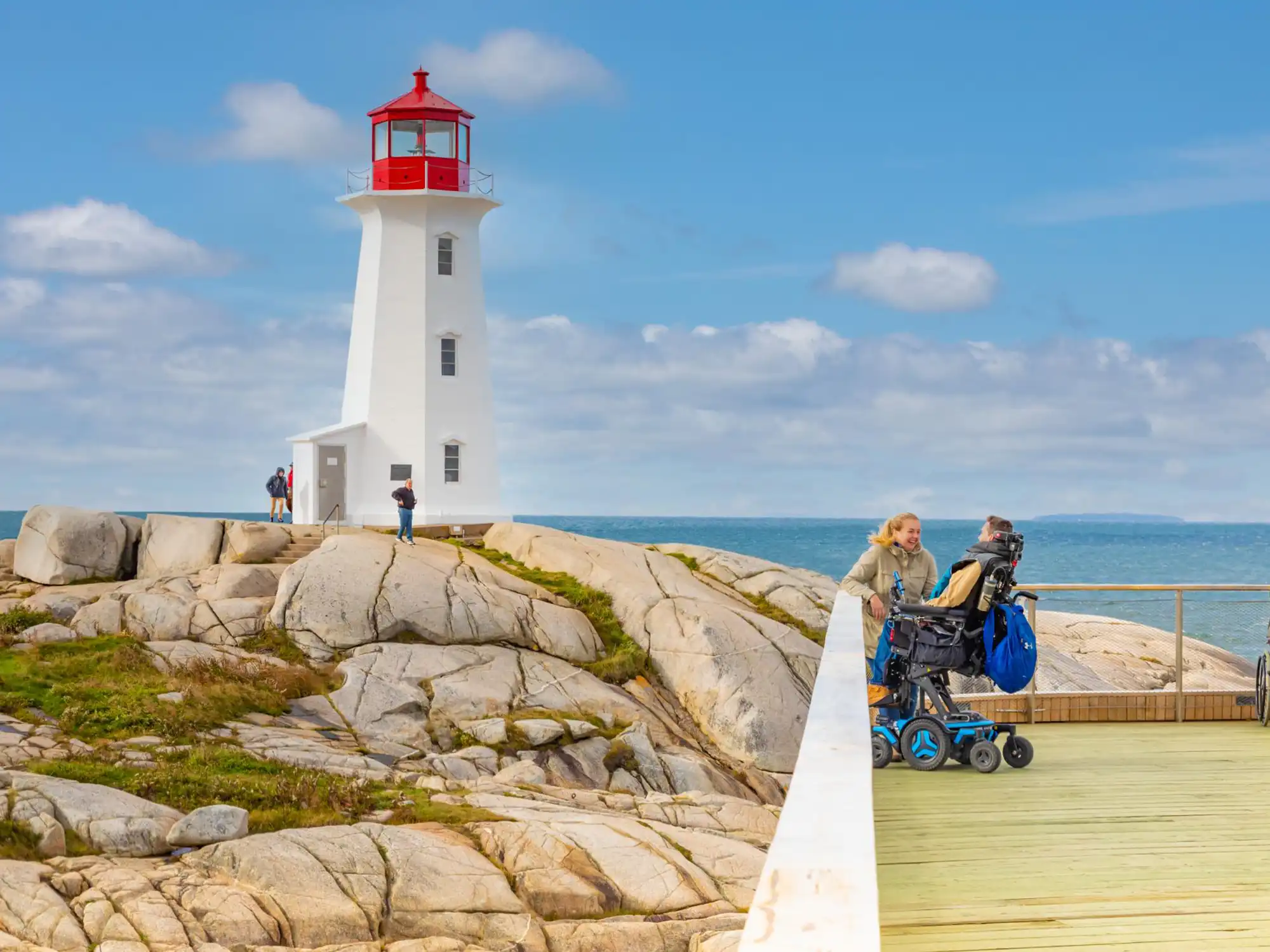 Peggy's Cove lighthouse with the accessible observation deck shown. On the deck is two people. one of which is a person in a wheelchair viewing the lighthouse.