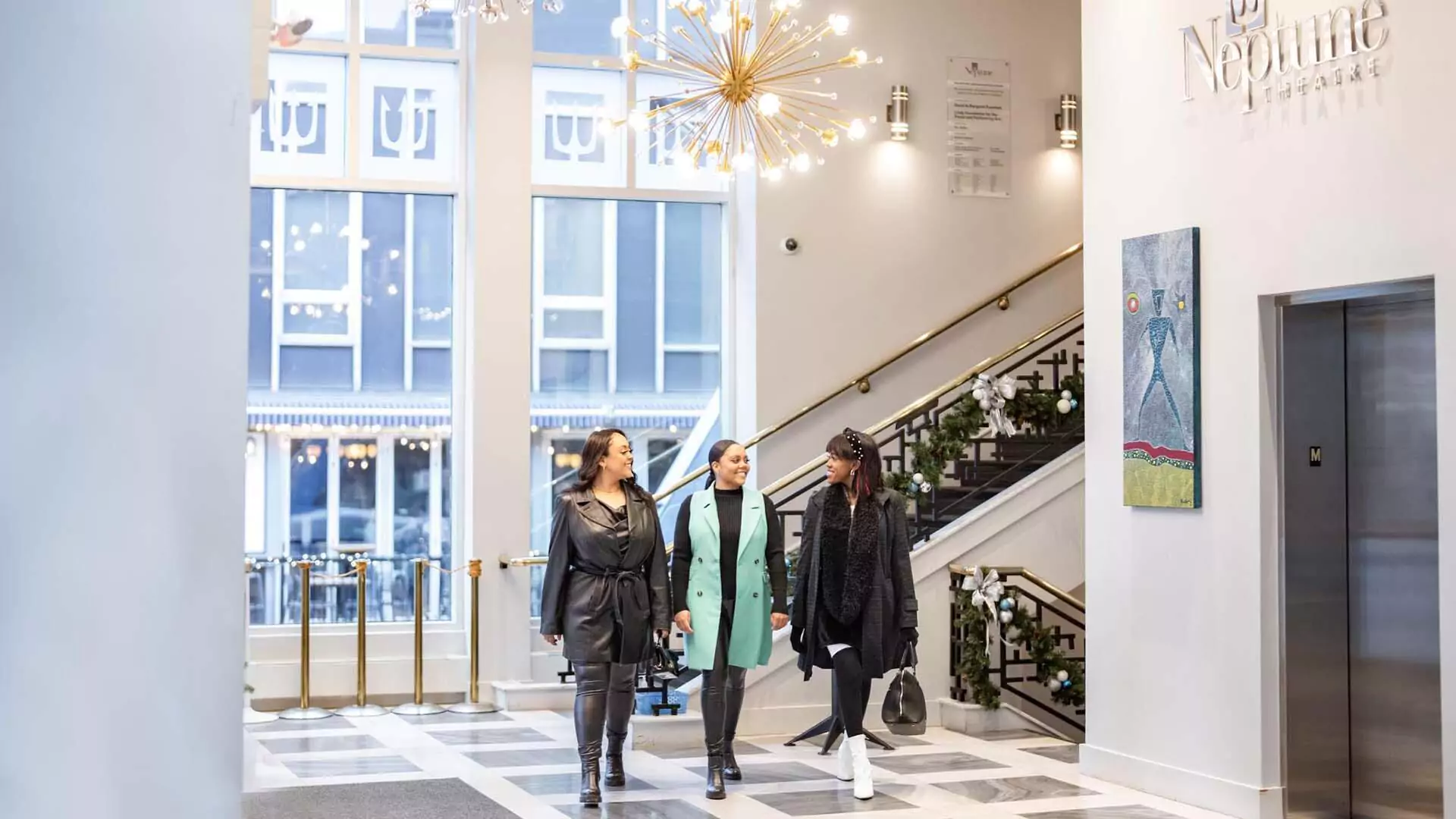 Three women walk into the bright lobby of Neptune Theatre.