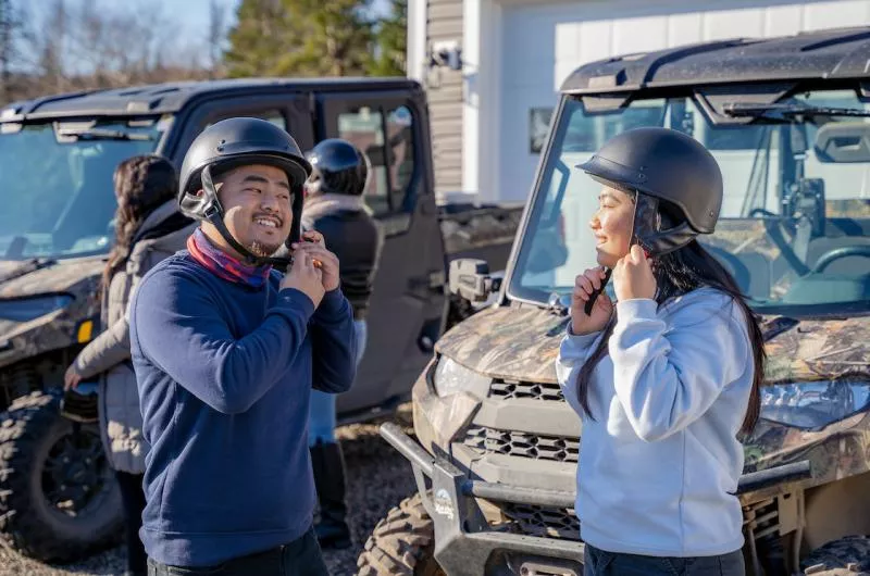 Two people buckle their helmets to prepare for a tour on a side by side.