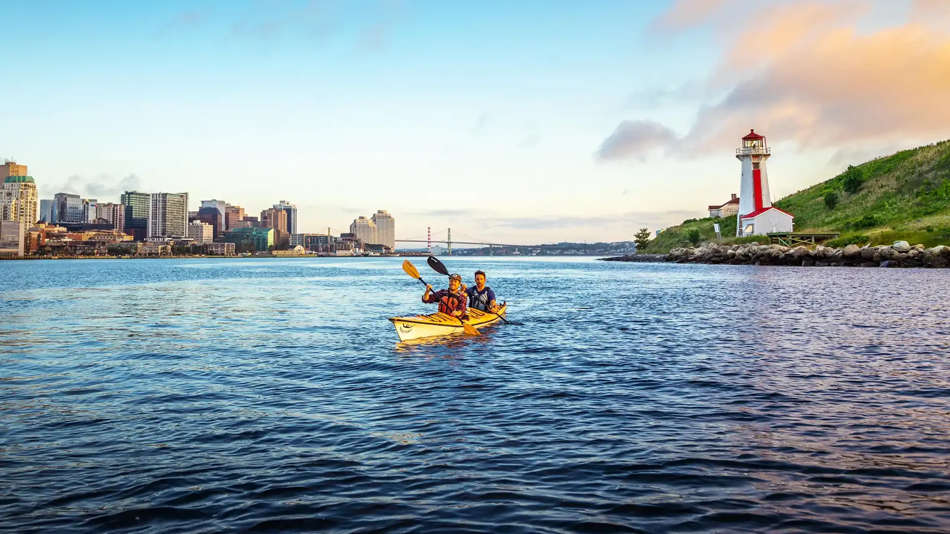 Two people kayak past Georges Island National Historic Site in the Halifax Harbour in Nova Scotia at sunset.