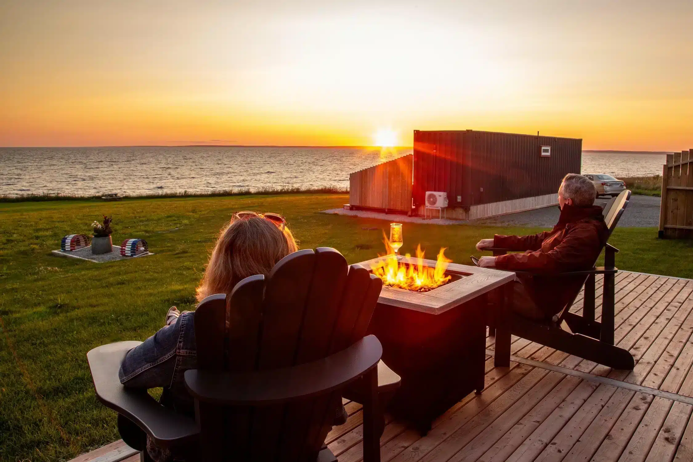 Woman sitting in a deck chair by a fire pit, looking at the sunset
