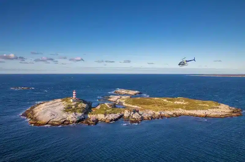 Aerial of a helicopter flying over a small island with a lighthouse.
