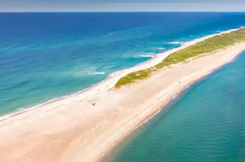 A long sandy piece of land sticks out into the very blue ocean. It is a sunny, blue sky day.