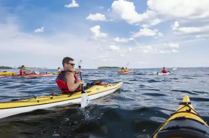 A large group of people kayak on the ocean. There is an island in the distance.