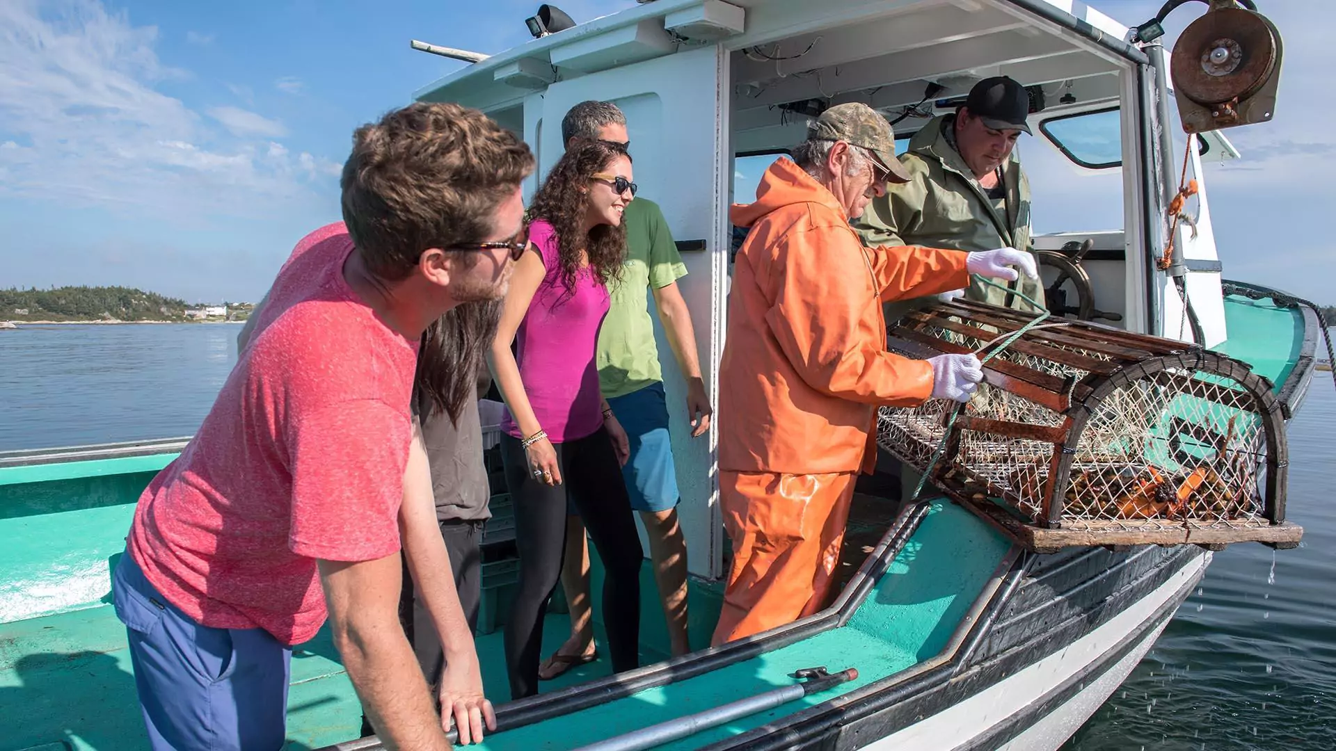 A group of visitors watch a fisherman remove a lobster from a trap on a lobster boat.