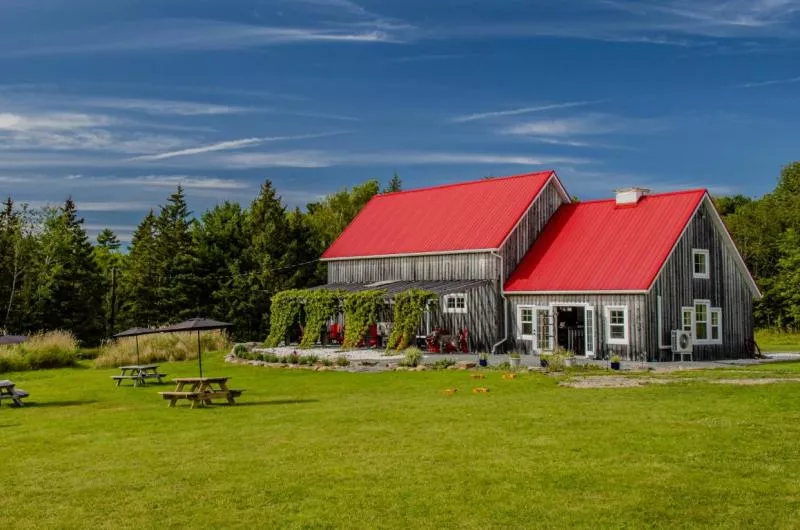 An old barn style building with a red roof is surrounded by green grass on a blue sky day.